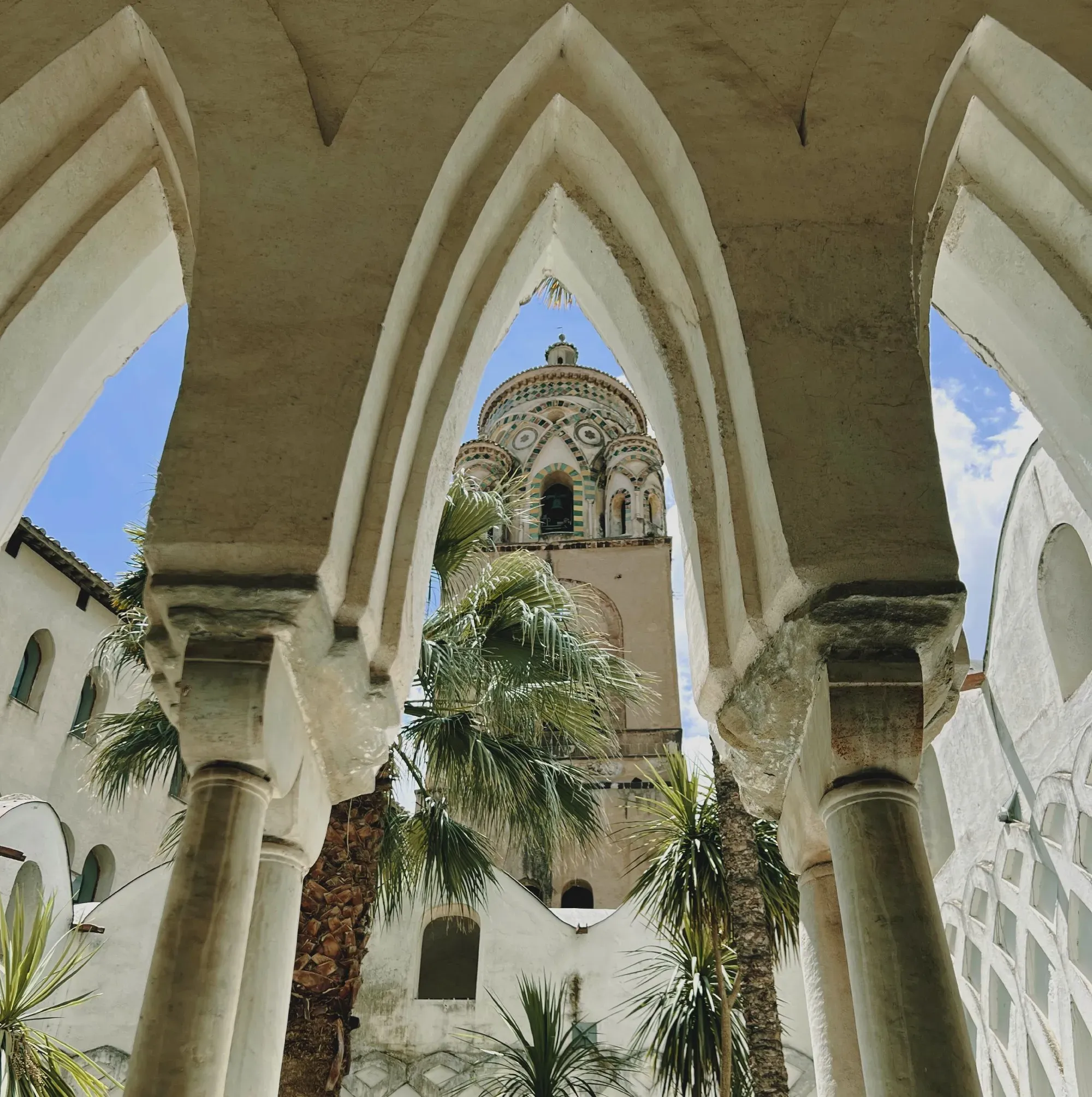 Artsy shot of the Amalfi cathedral's steeple, framed between pointed arches and columns.