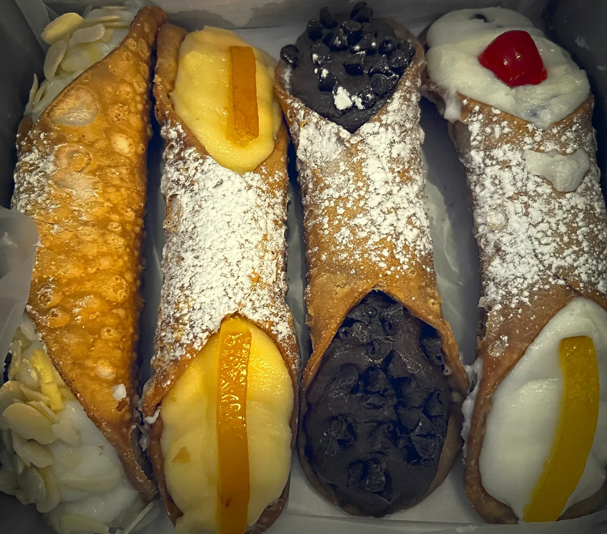Canolli. Four canolli in a pastry box. Almond, orange, chocolate, and classic flavors.