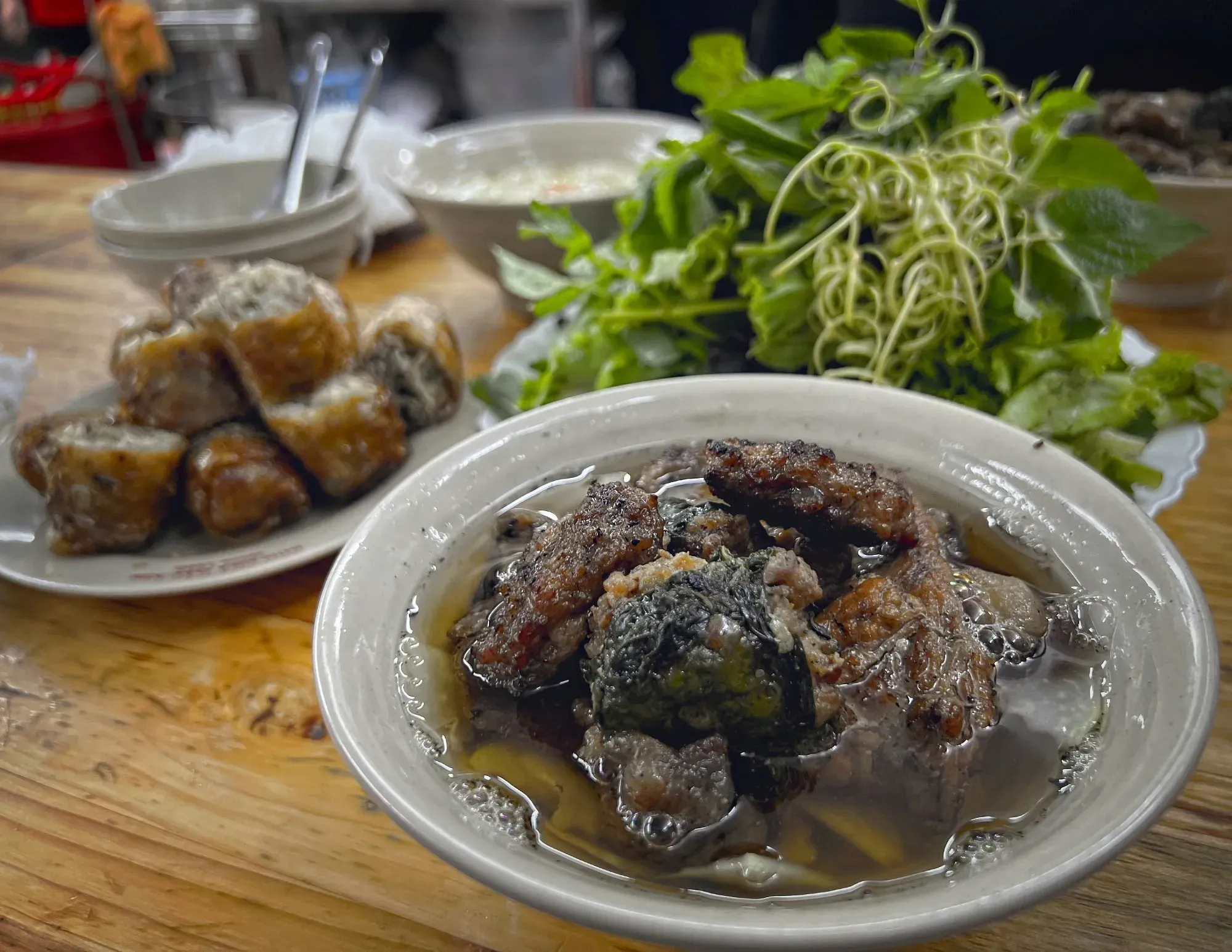 Bowl of Bún chả with herbs and nem cua bể in the background.