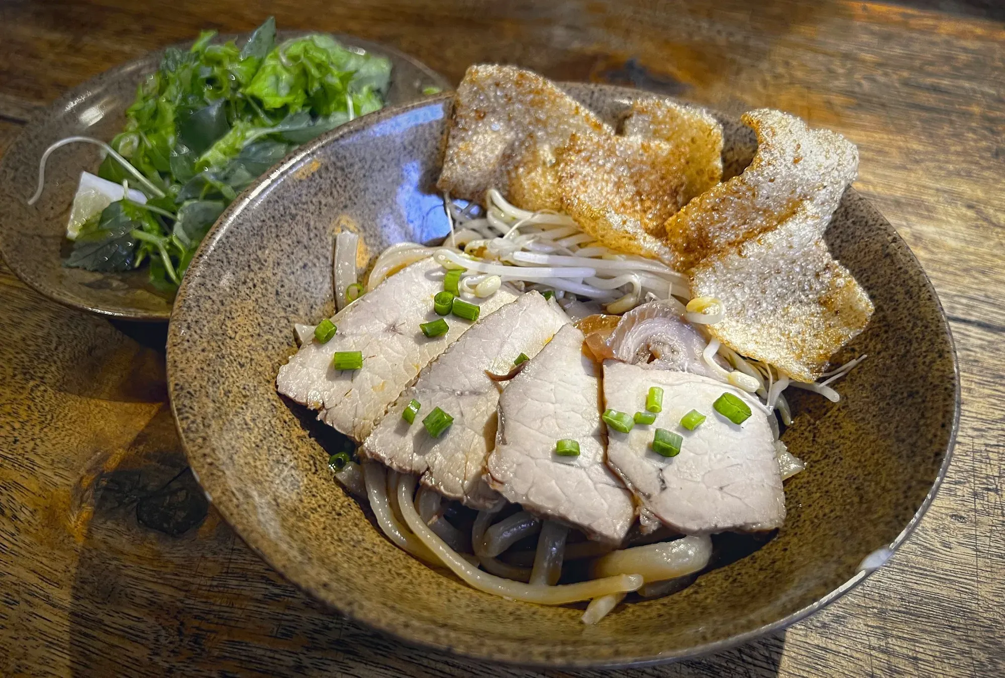 Bowl of Cao Lầu with garnishes in background.