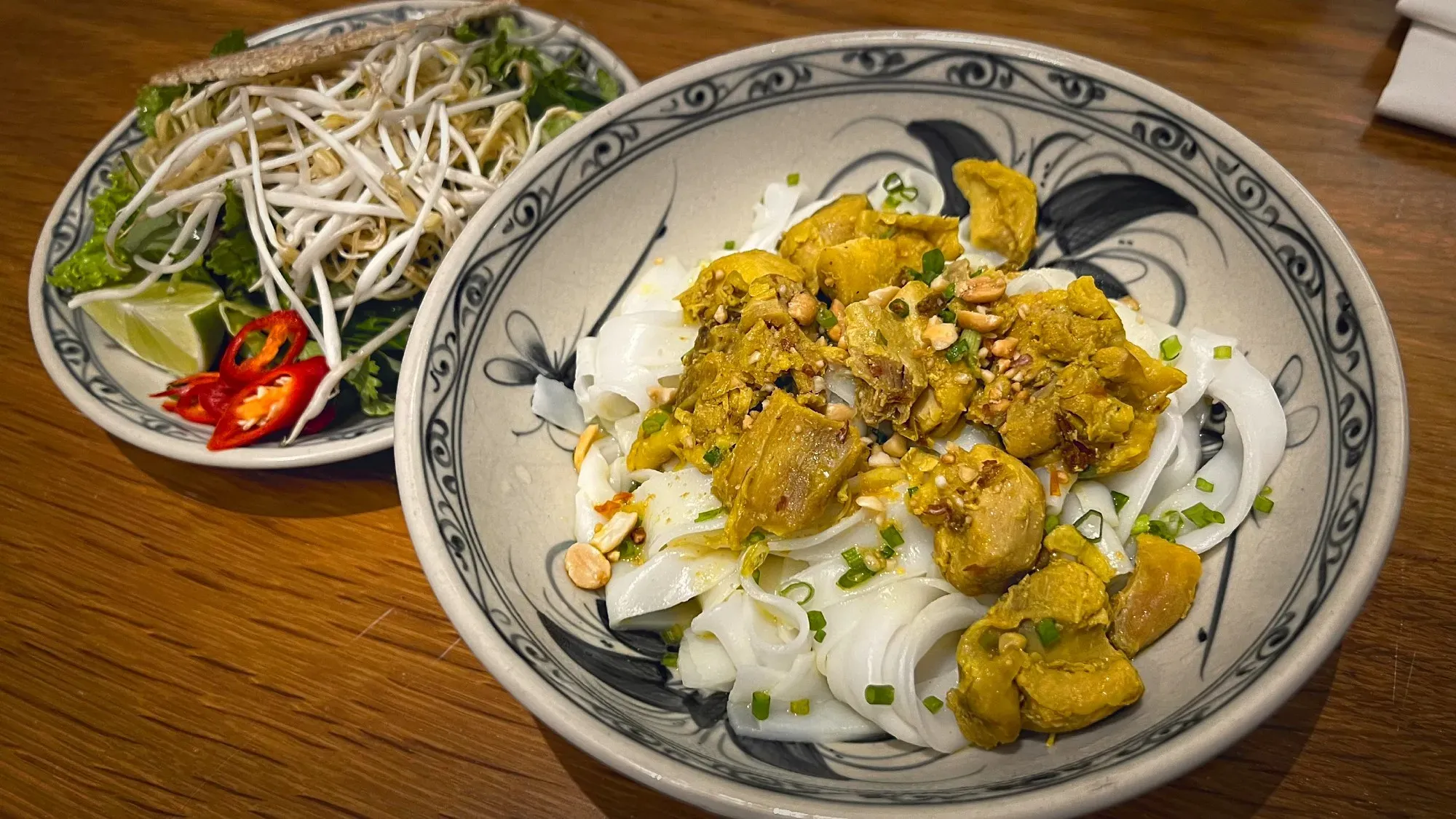 Bowl of Mì Quảng with garnishes in background.