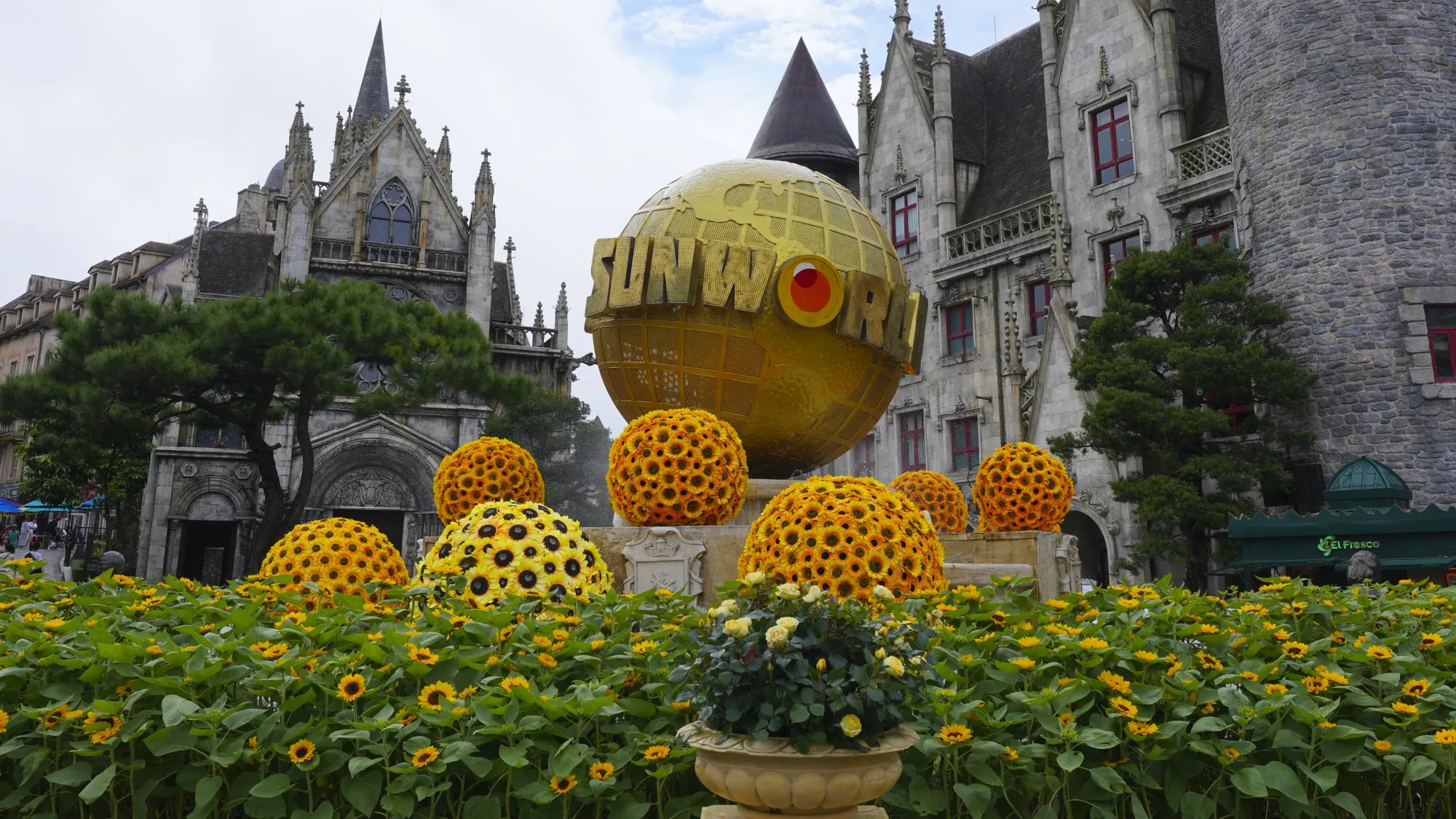 Golden Globe with "Sun World" written on it with sun flowers around it and a castle in the background