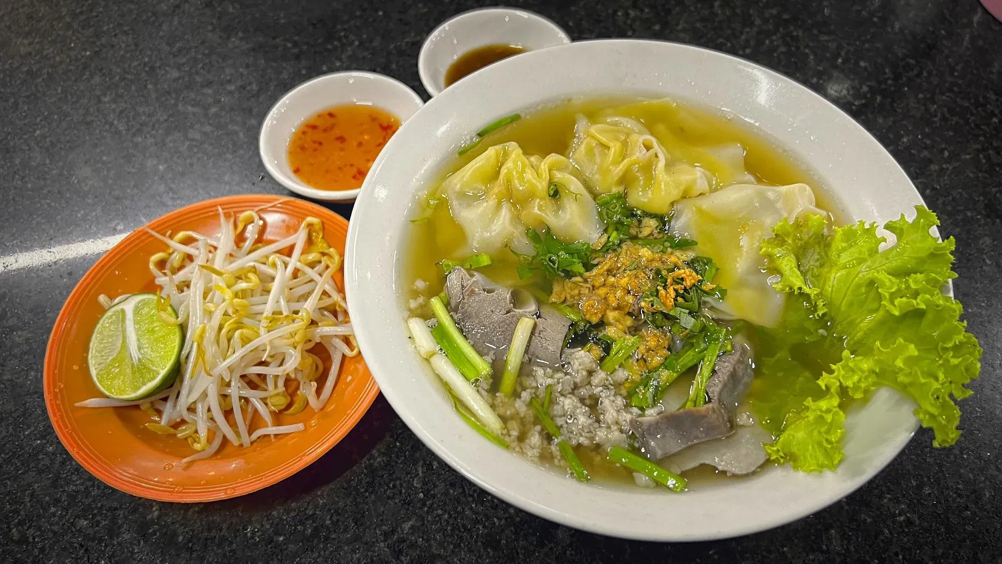 Bowl of Kuy Teav with a side of bean sprouts and a lime wedge.