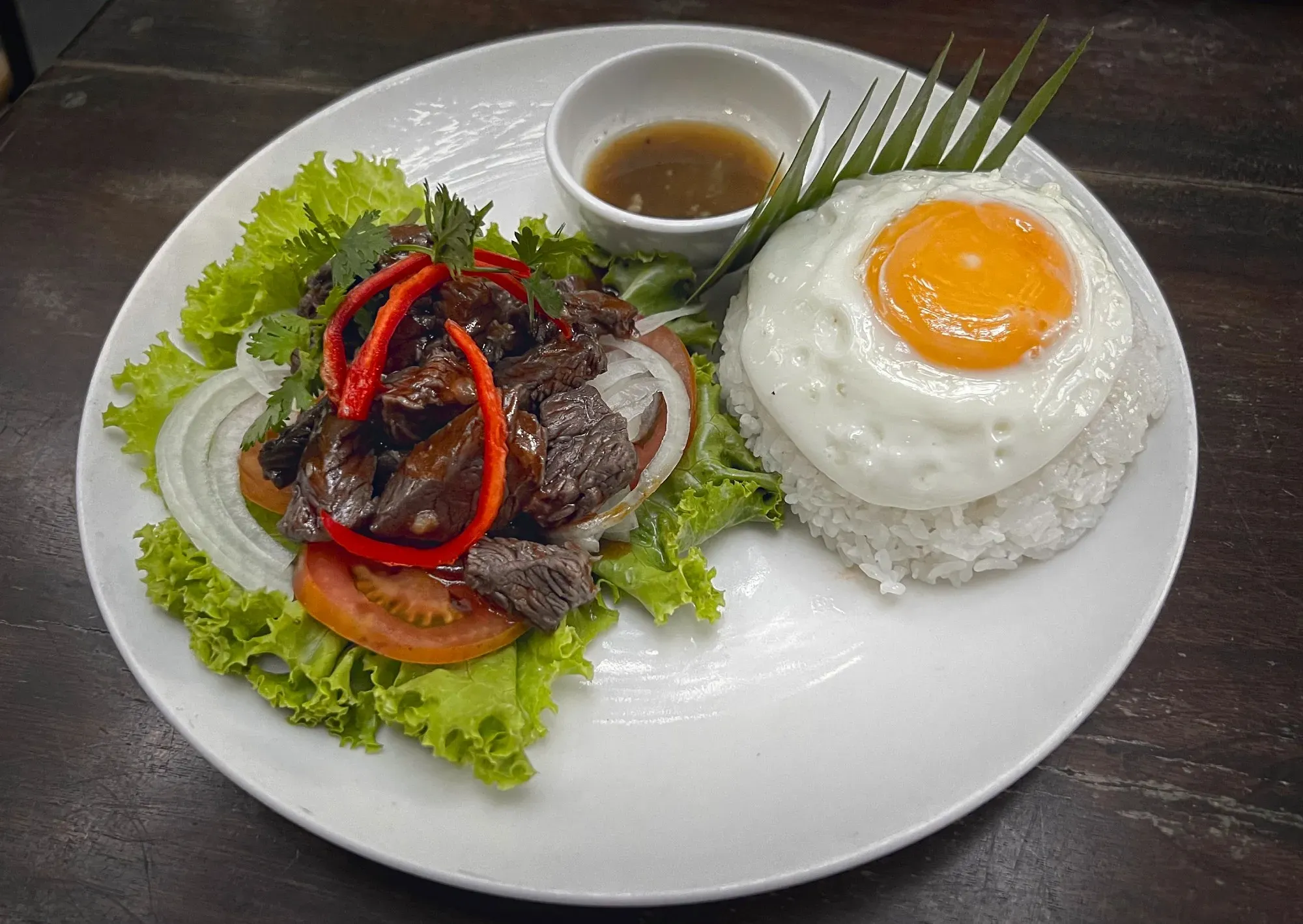 Lok Lak served on a bed of lettuce with rice and a fried egg.