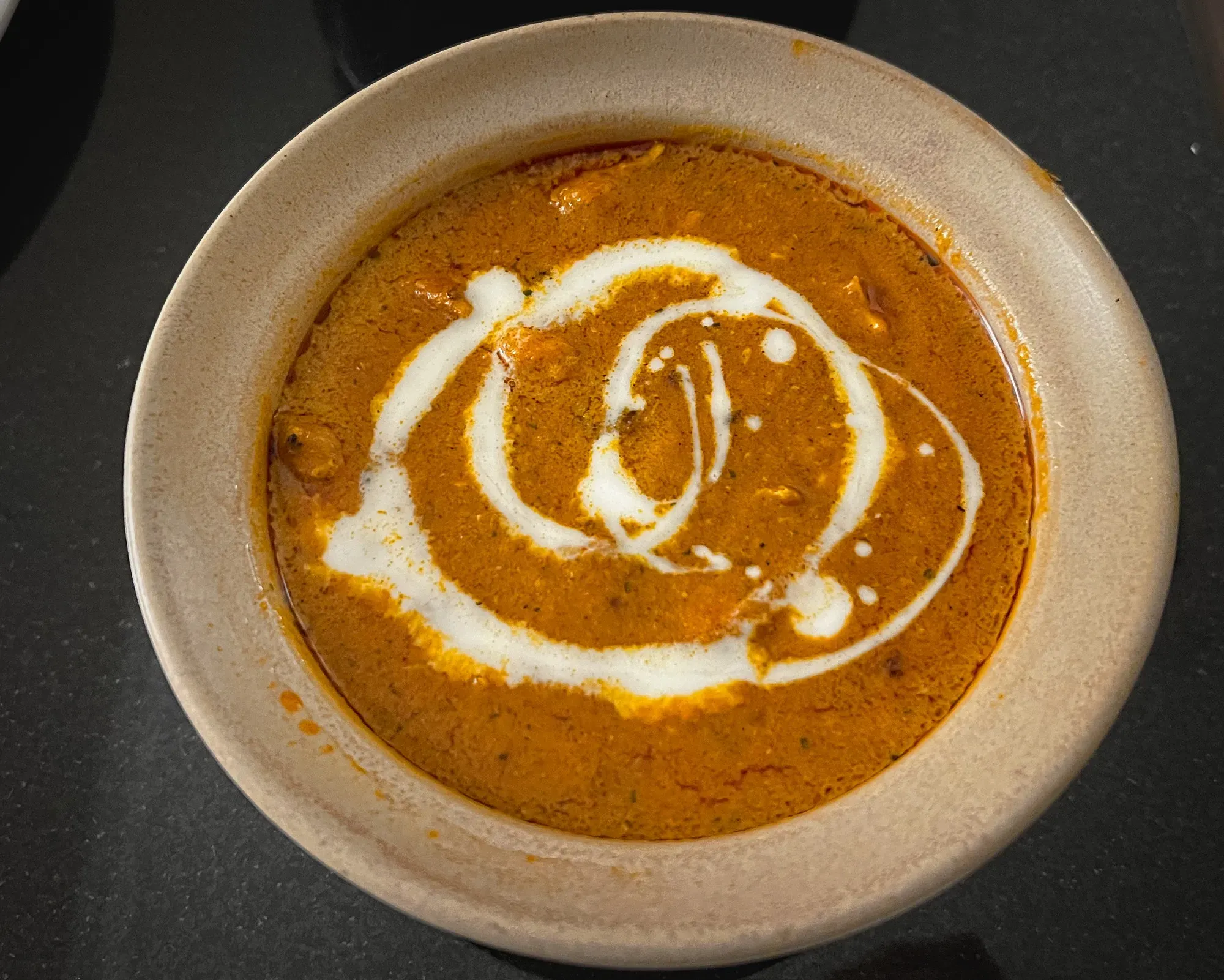 Close up overhead shot of butter chicken in a clay bowl.