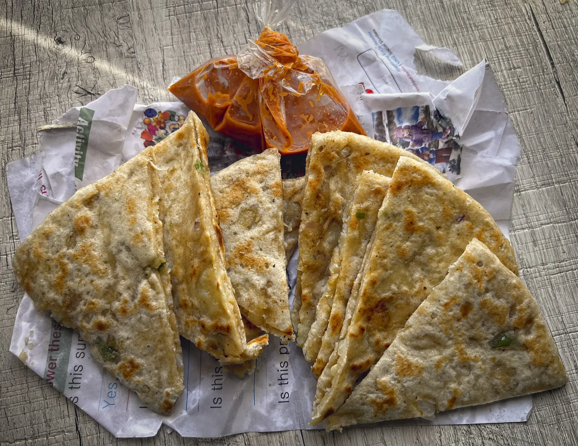 Paratha on newspaper with bags of dip, overhead shot.