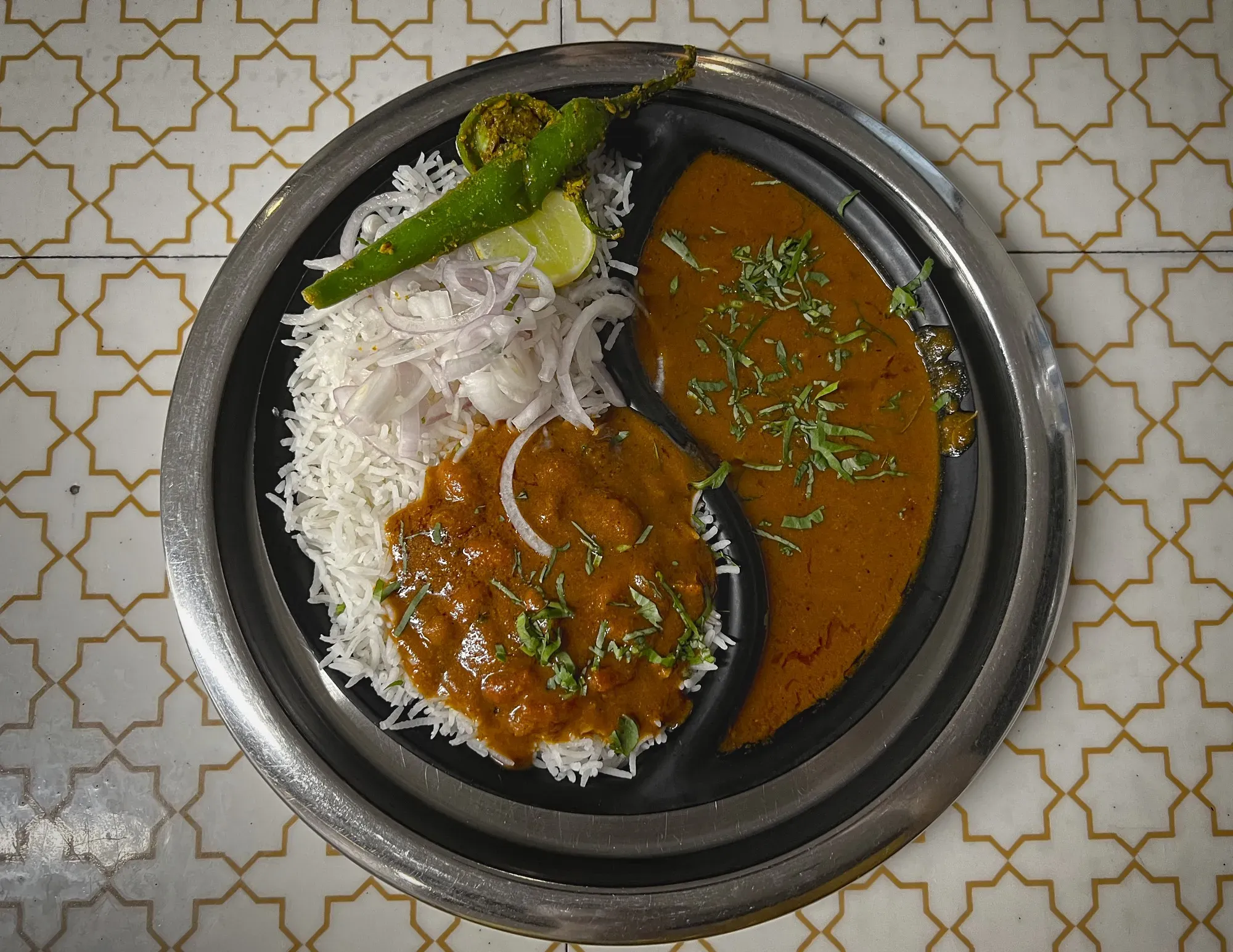 Overhead shot of a ying-and-yang shaped tray with Rajma Chawal on one side, and rice plus toppings on the other.