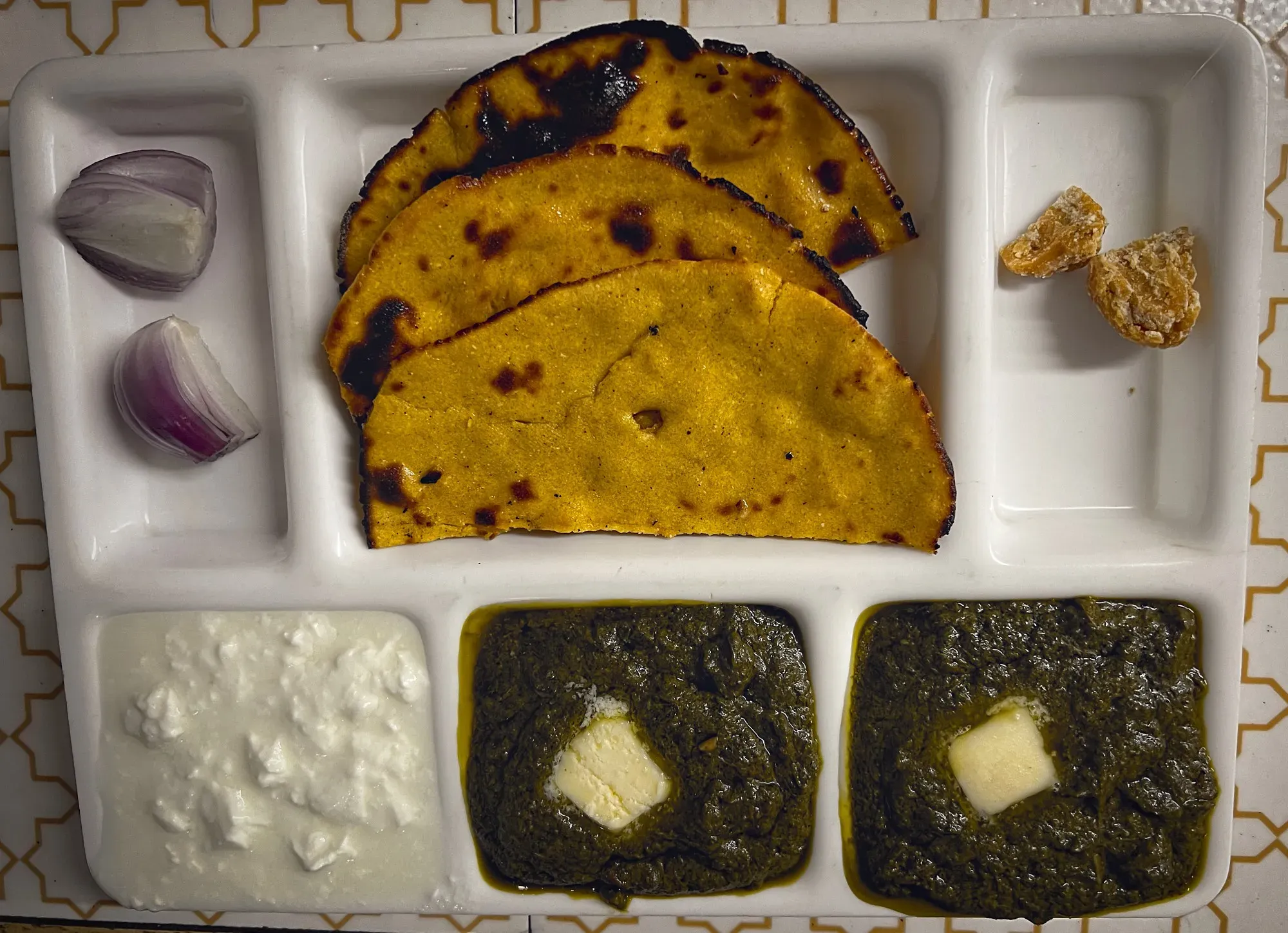Tray with two helpings of Saag with butter on top, a helping of yogurt, and 3 pieces of Makke Ki Rotti. Overhead shot.
