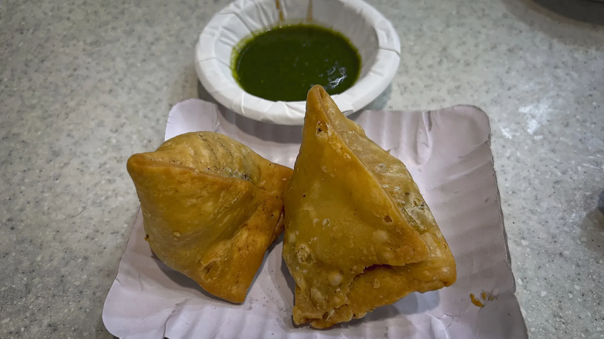 Two Samosa with a chutney dip in the background, angled shot.