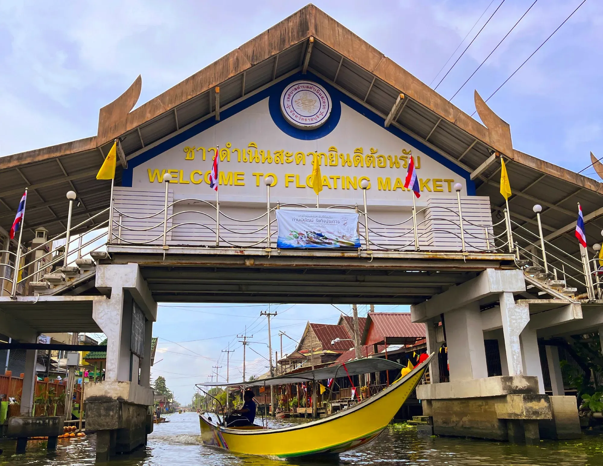 Yellow motor boat foating under walking bridge indicating the entrance to the Floating Market