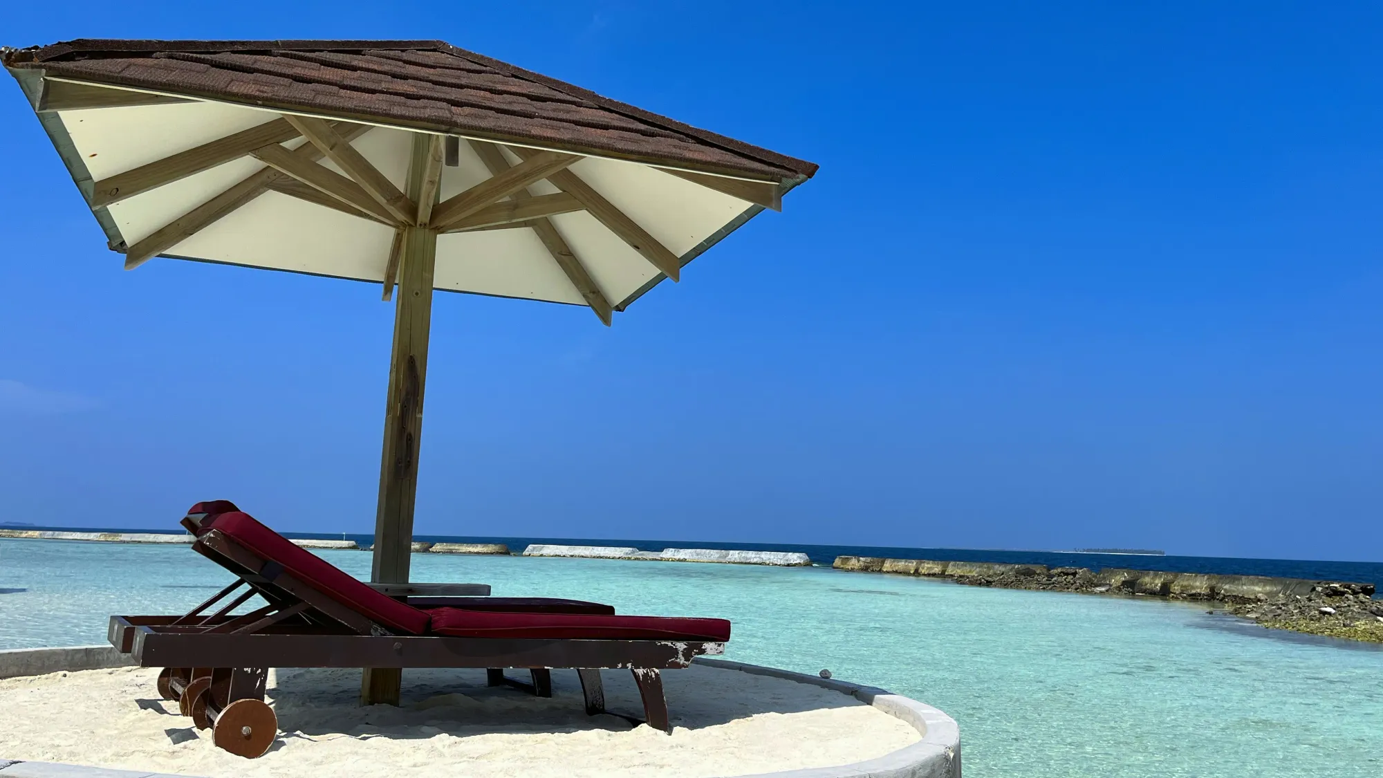 Two beach chairs under an umbrella overlooking the turquise water