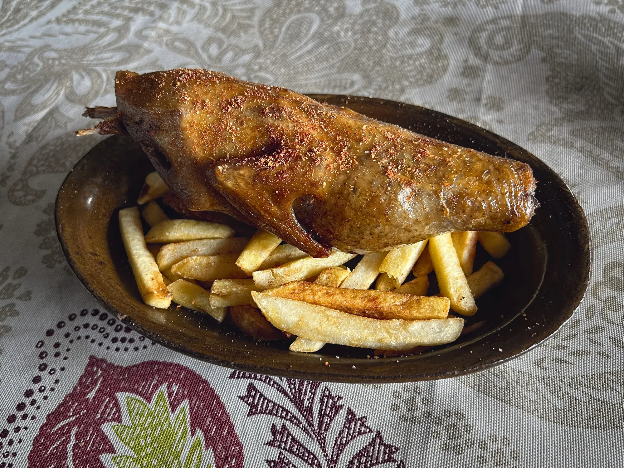 A whole stuffed pigeon lying on a bed of fries, table shot.
