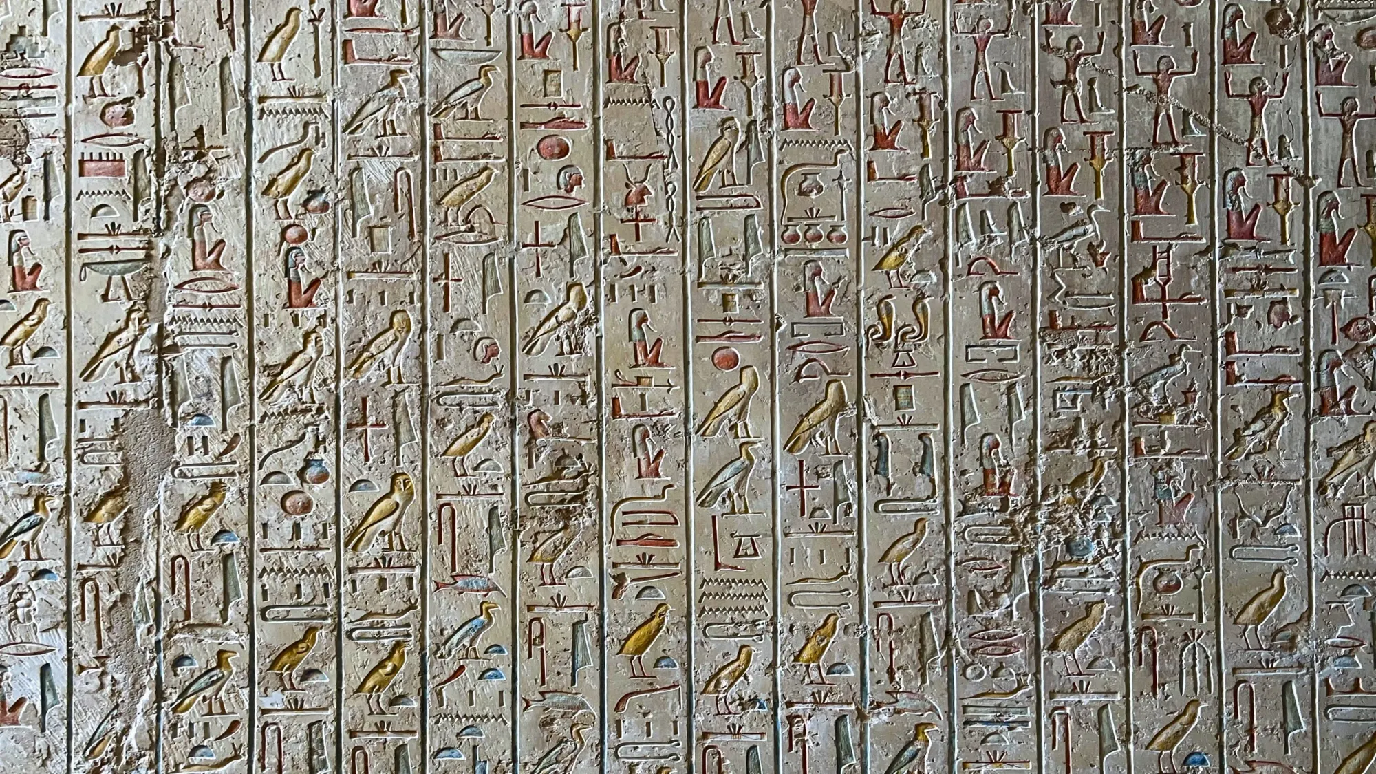 White wall with painted hieroglyphics in yellows, reds, and blues