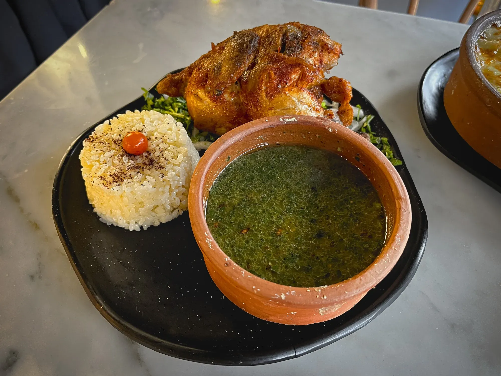 Molokhia in a clay pot with a side of rice and chicken, angled shot.