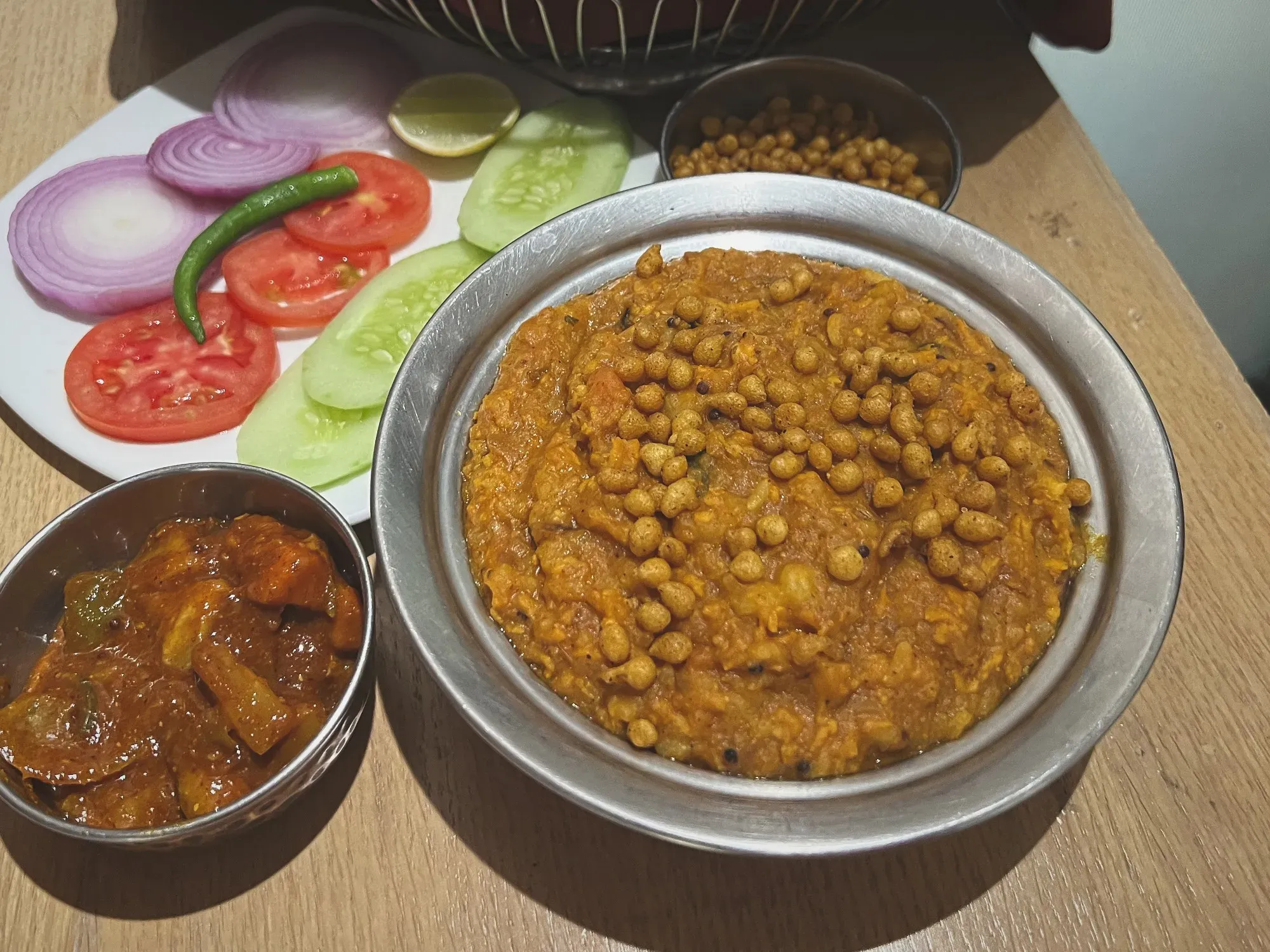 Angled shot of a bowl of bisi bele bath with sides of fermented and fresh vegetables.