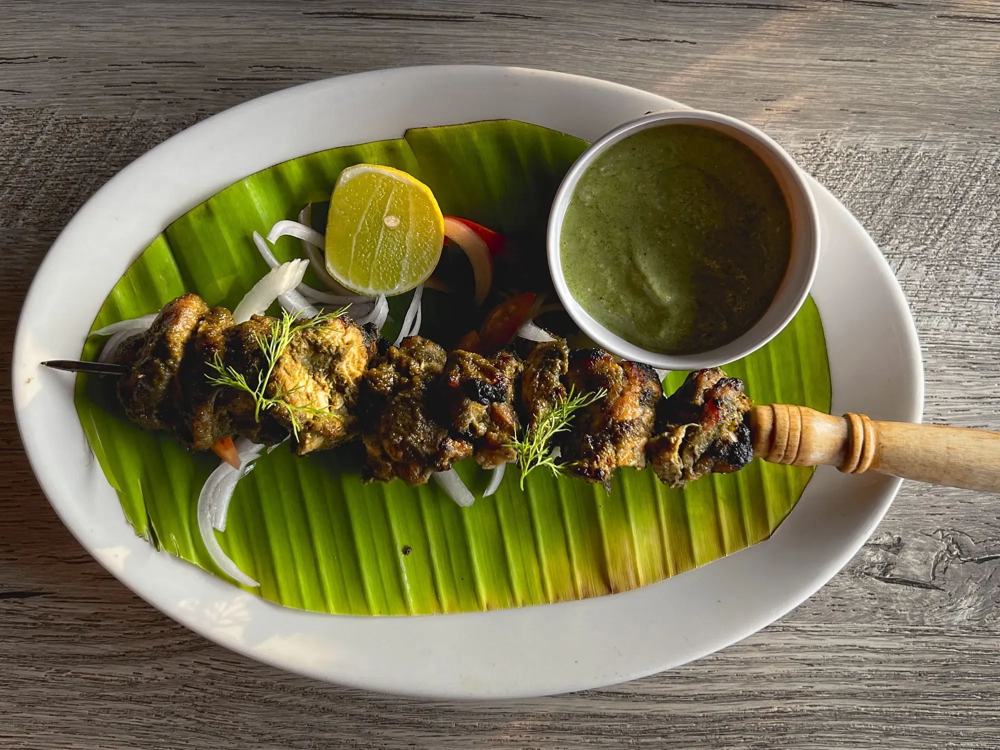 Frango à Cafreal on a skewer with a dipping bowl of sauce, overhead shot.