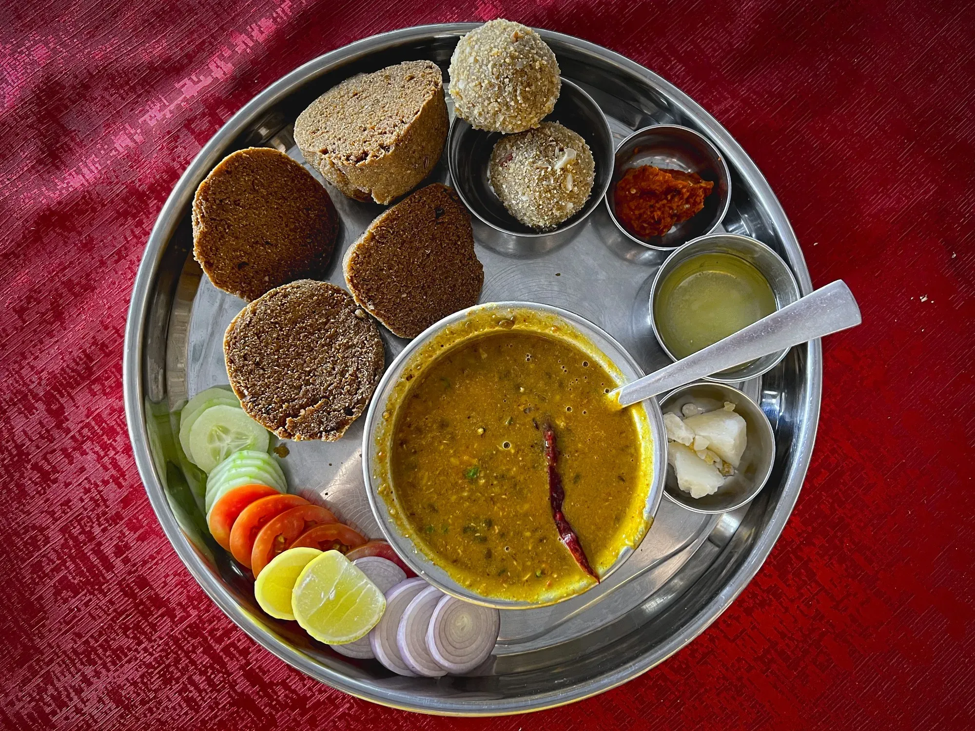 A tray with a serving of Dal Baati and two Charm cut in halves with additional sides. Overhead shot.