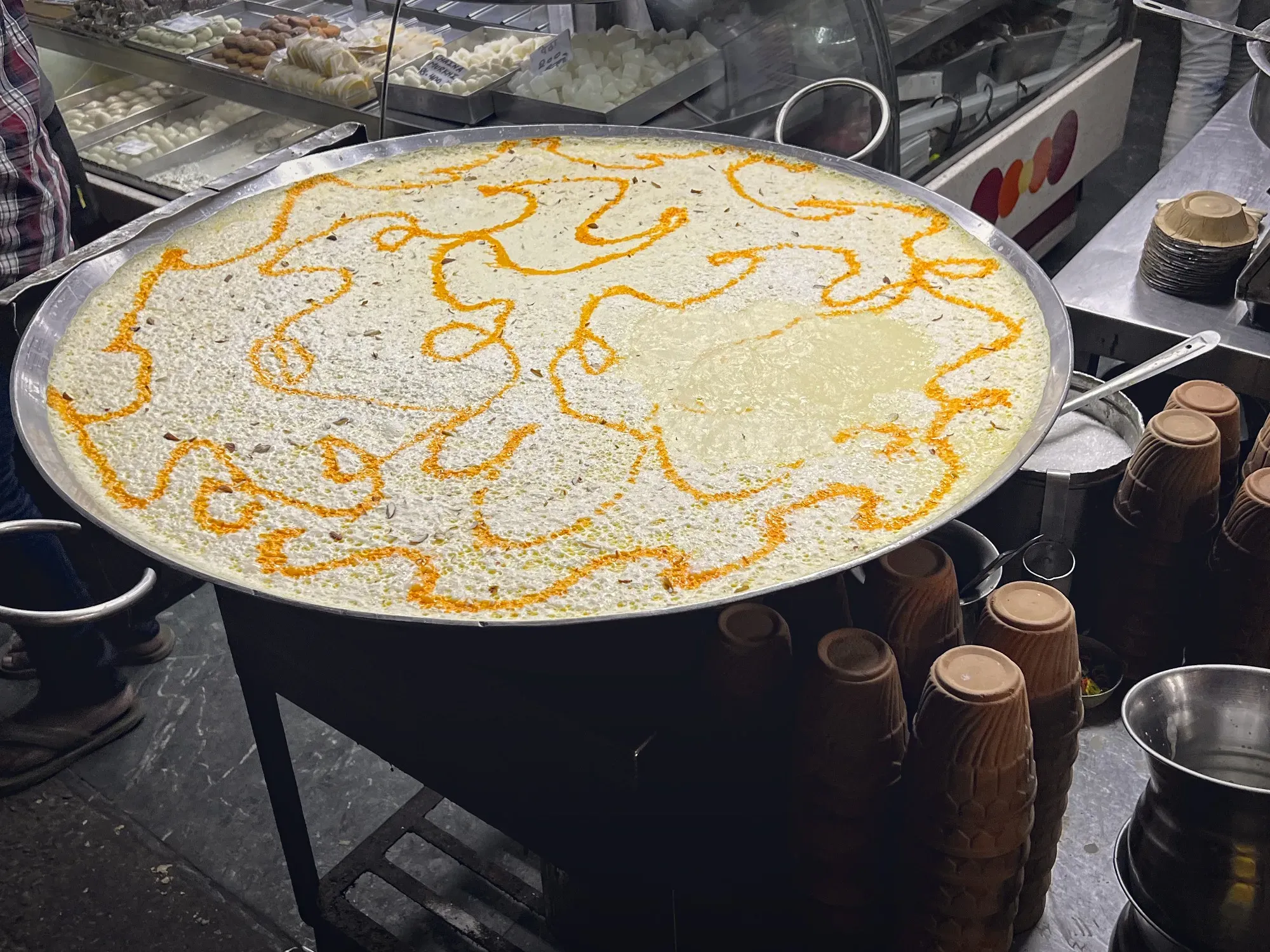 Huge pot of Kheer in the street outside a sweet shop in India with a stack of small clap cups for serving.