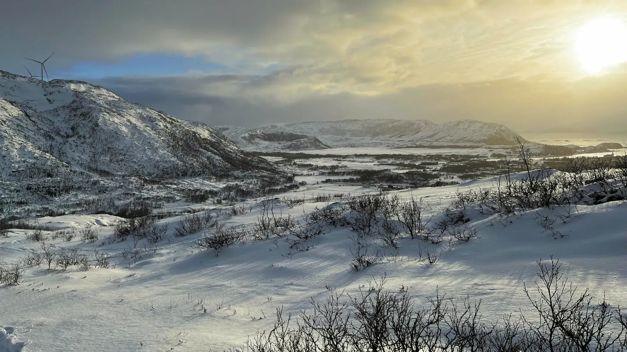 Sun shining over snow covered hills with windmills in the background