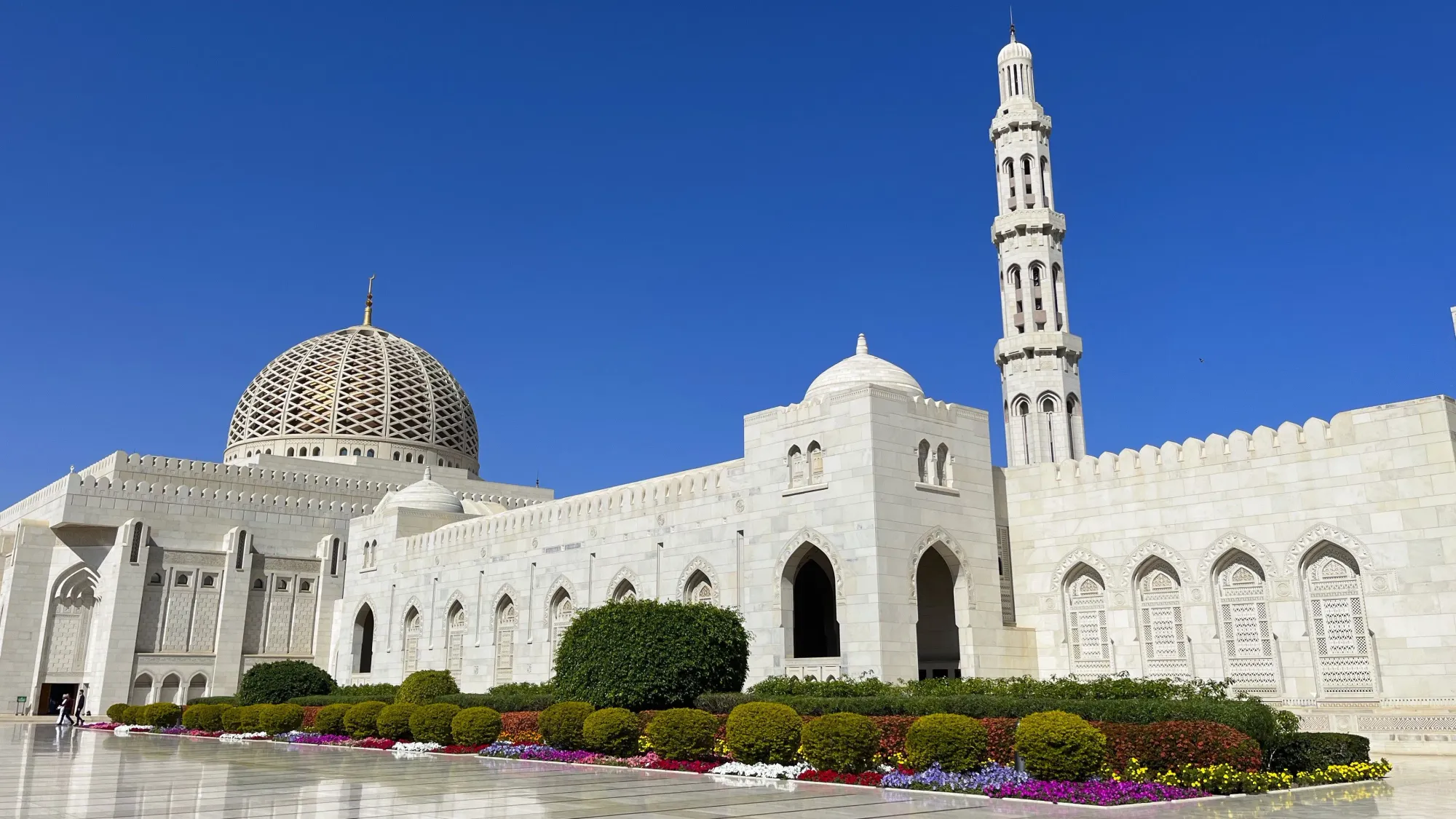 White exterior of the Sultan Qaboos Grand Mosque with a colorful flowerbed in front of it