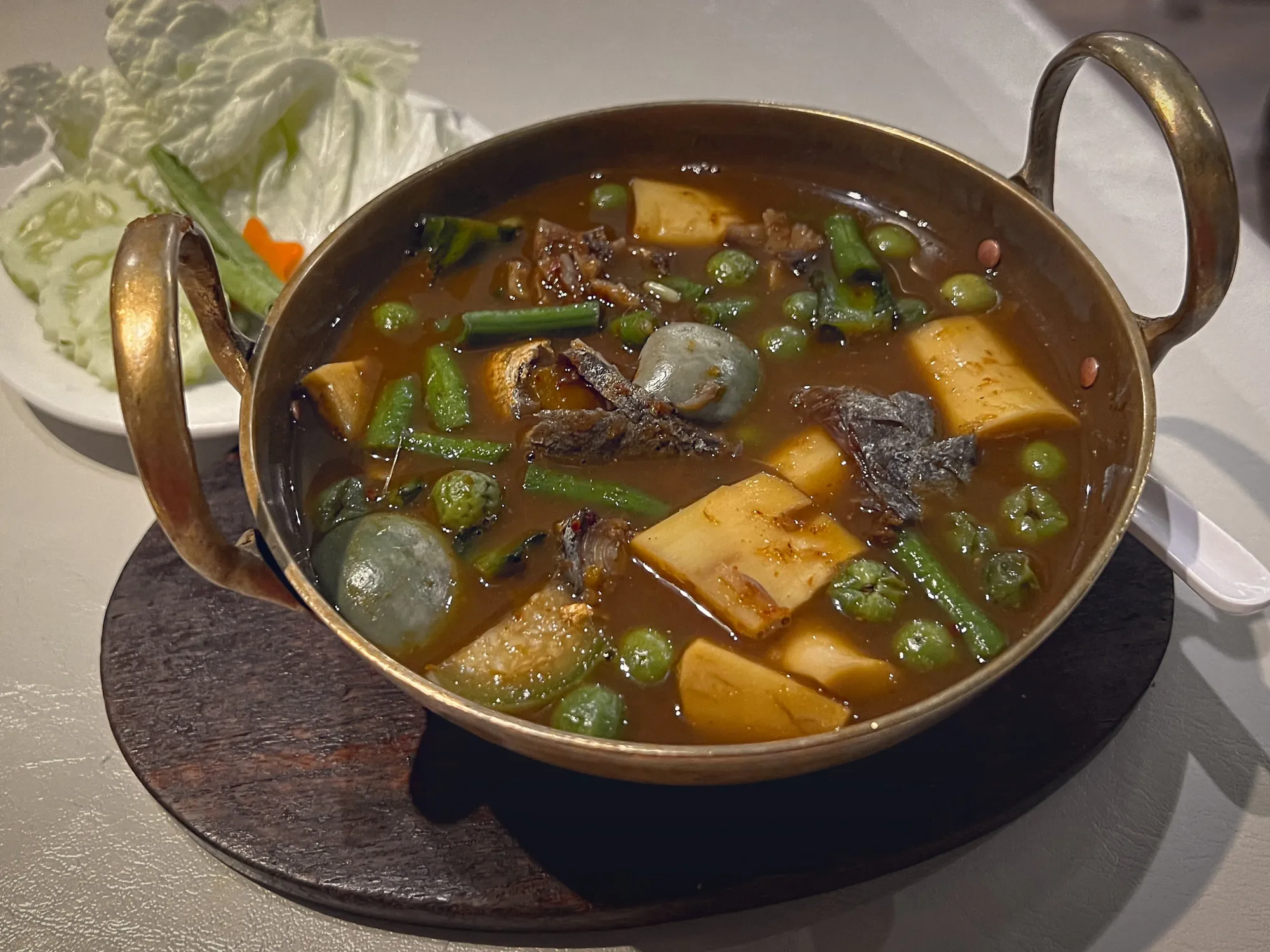 Kaeng Som in a metal serving bowl, angled shot.