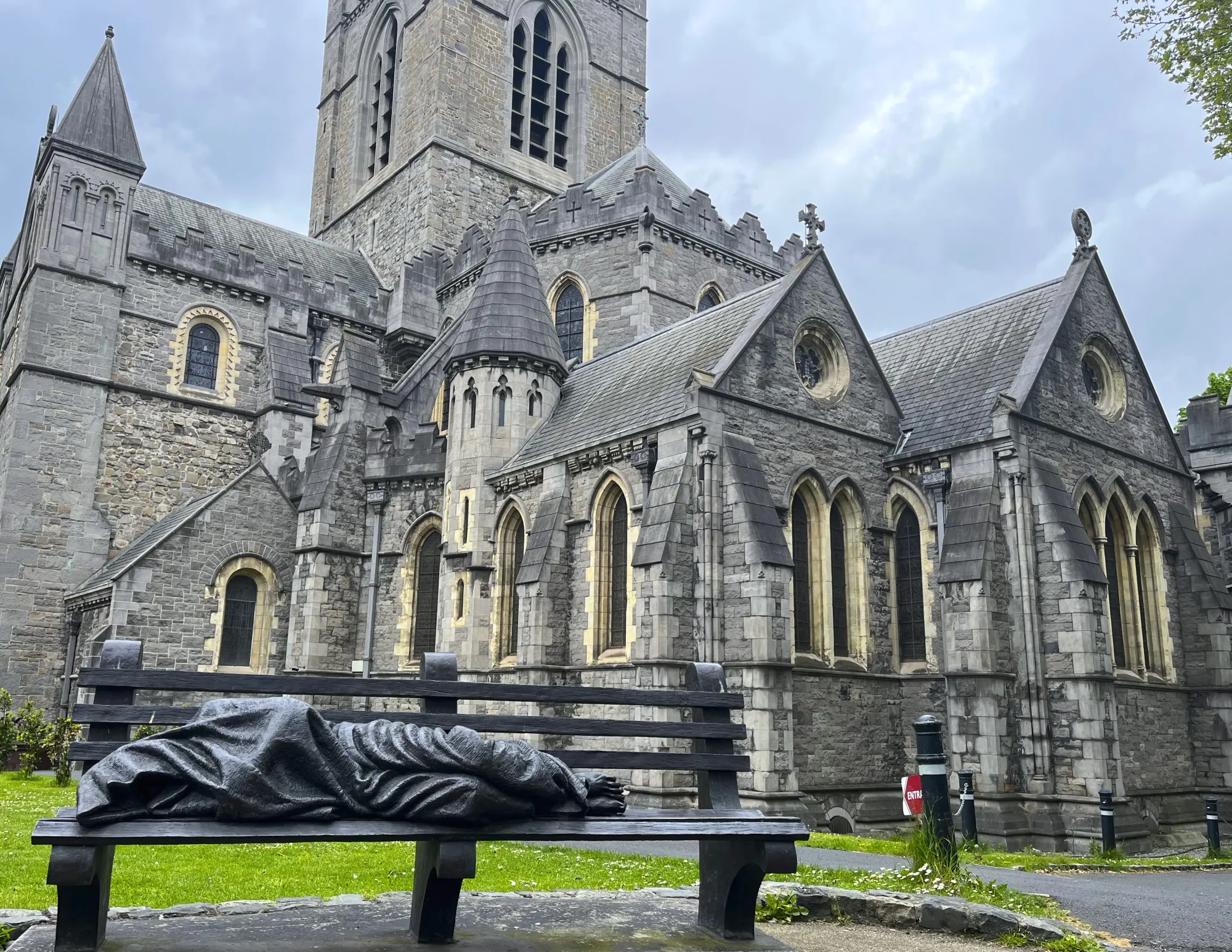 Statue of a wrapped figure laying on a bench in front of a grey stone cathedral
