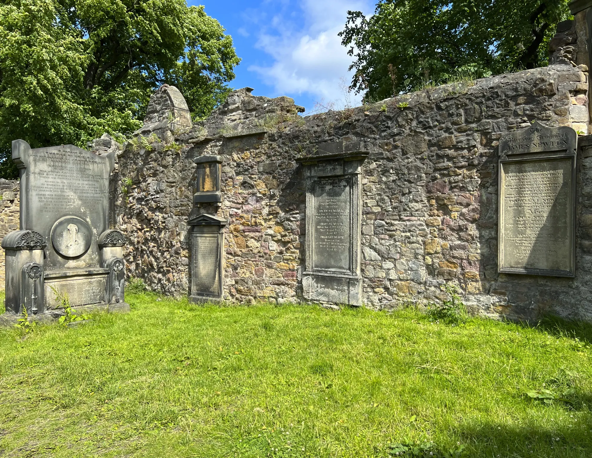 Green cemetery with tombstones embedded in a stone wall
