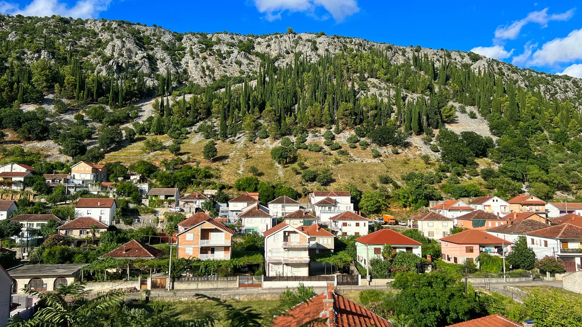 Warm colored houses nestled into the foot of a grey stone mountain lined with trees