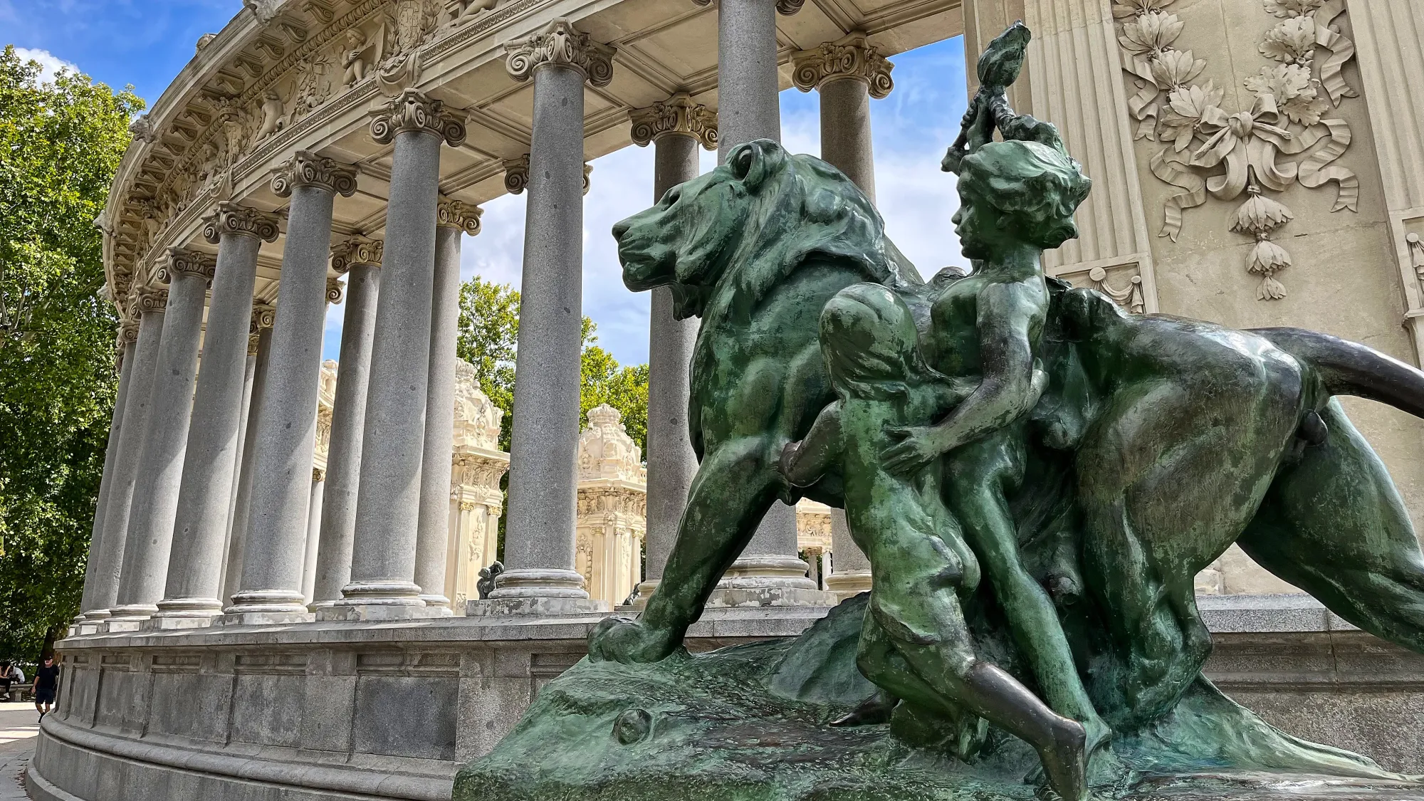 Statue of a lion and two children in front of a curved row of columns