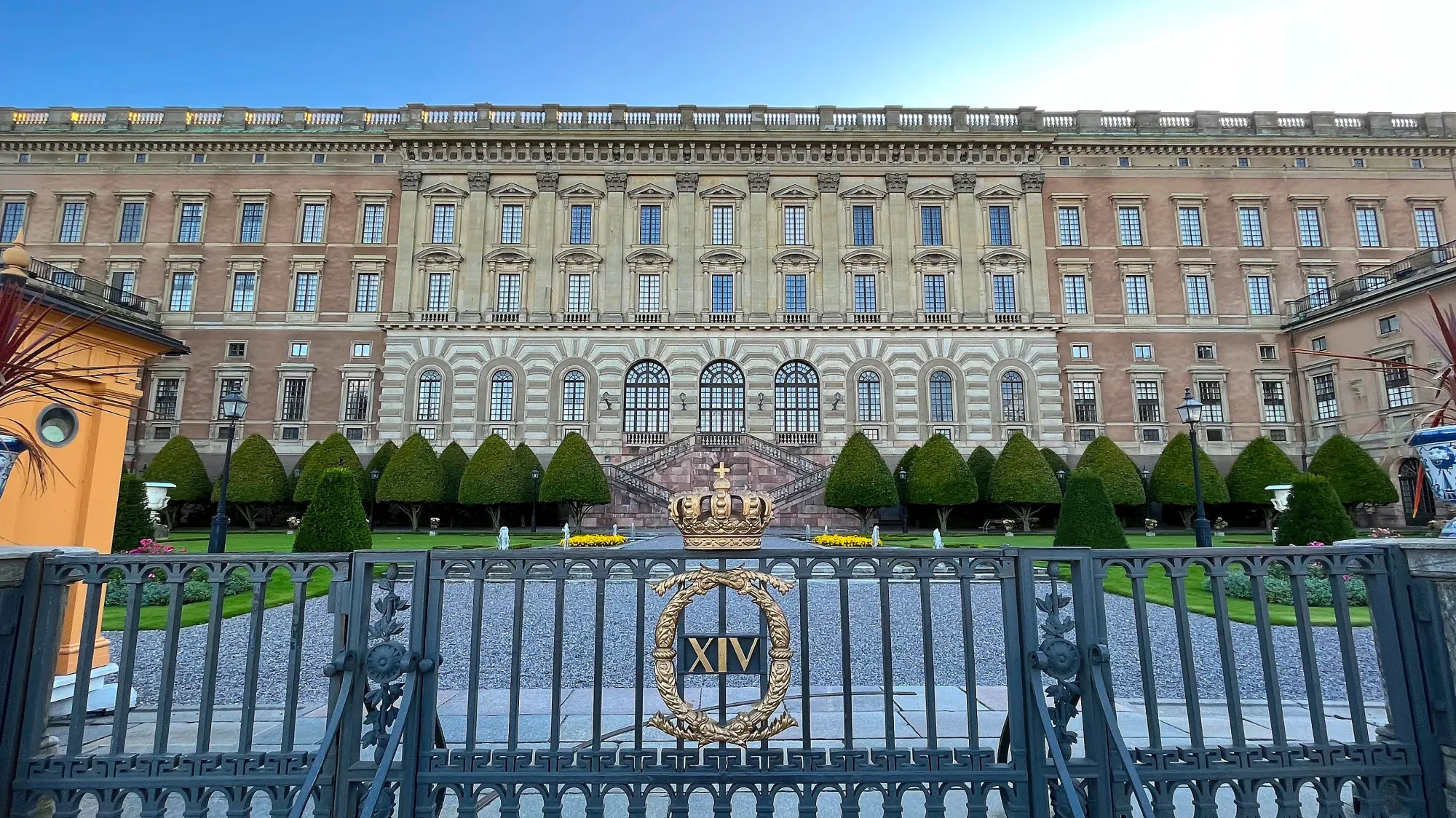 Heavily windowed facade with a black gate and golden crest in the forefront