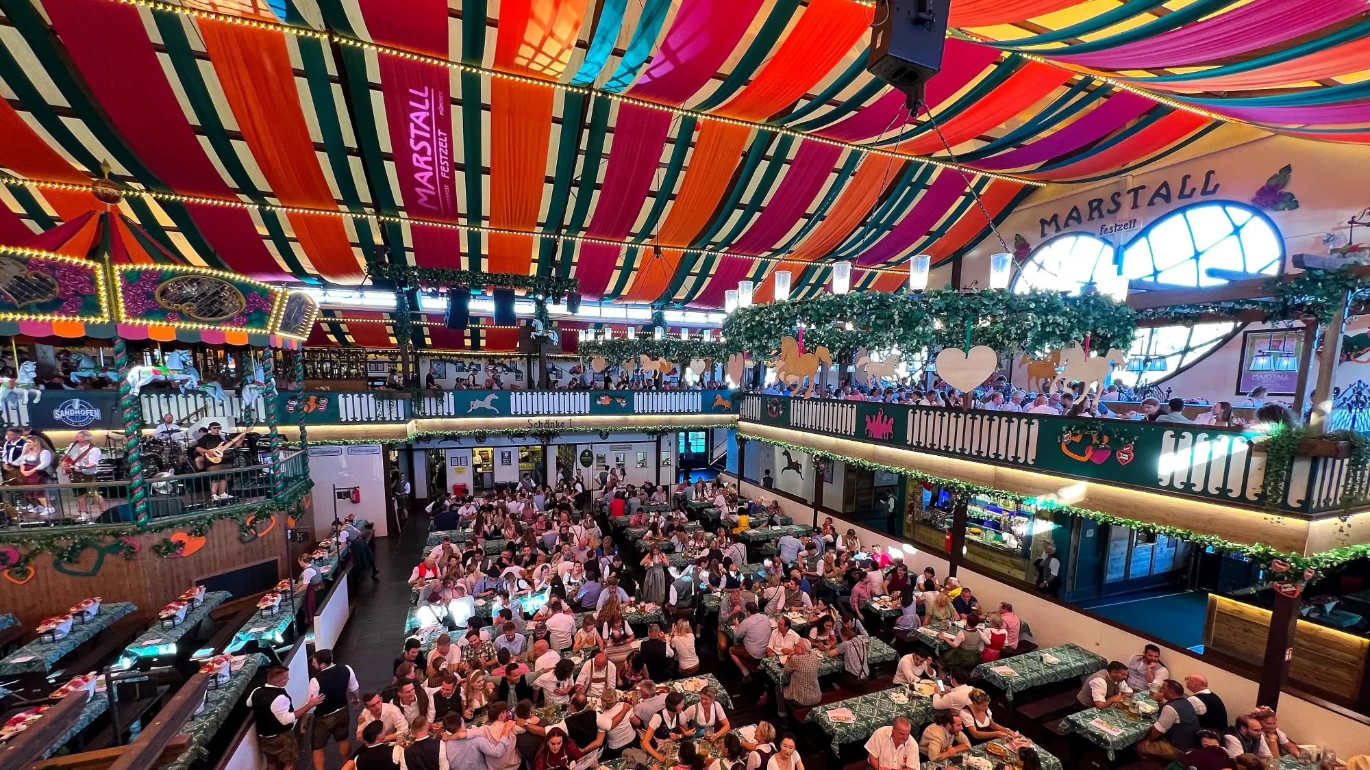 Two story tent filled with people drinking at the tables and with a pink/orange streamer covered ceiling