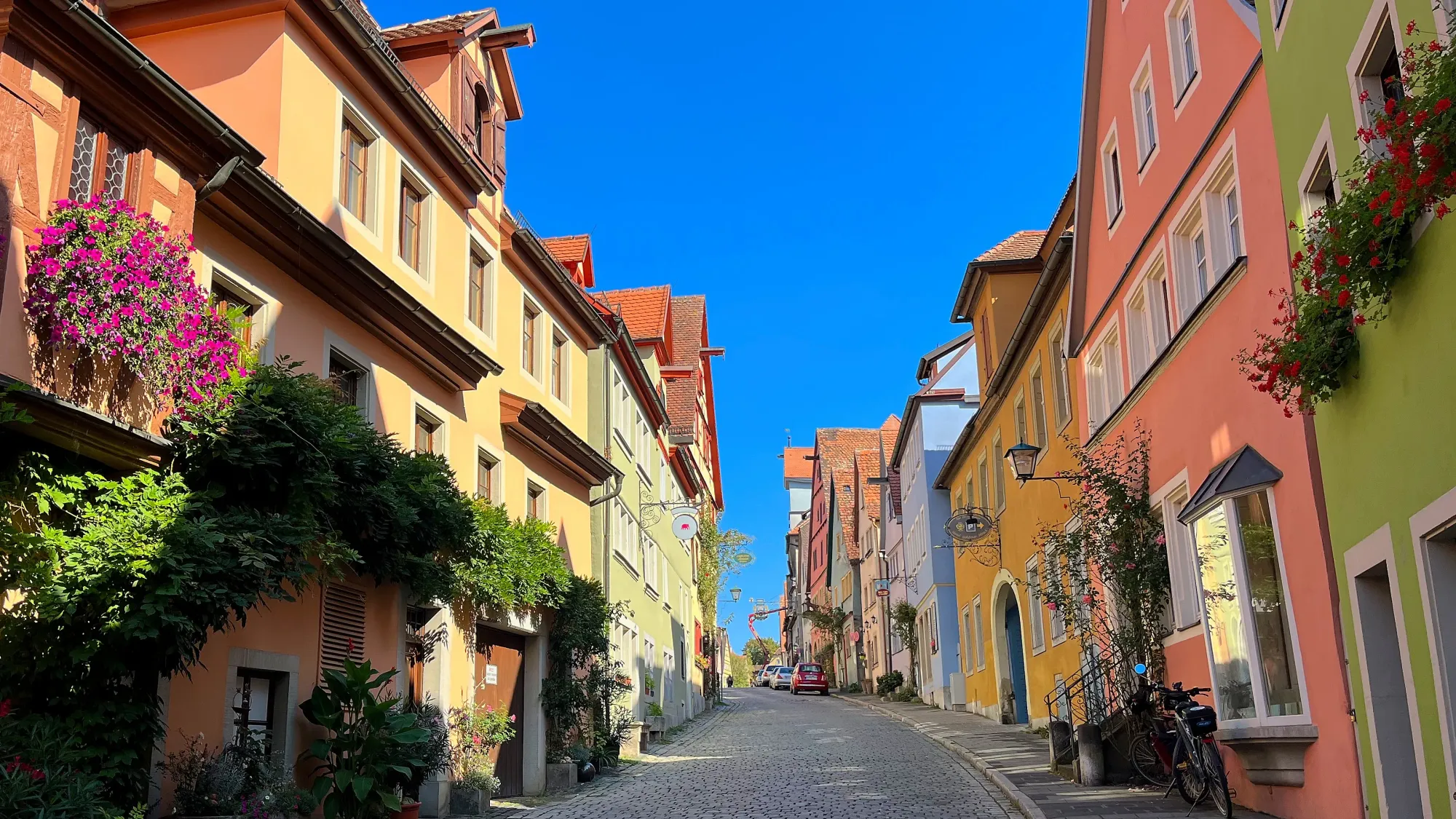 Pink, green, and yellow buildings filled with flower boxes on either side of an empty street