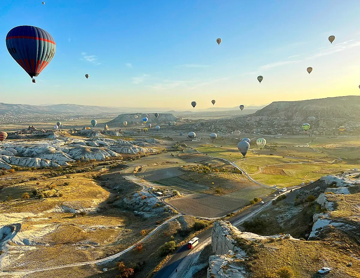 Green valley with white cliffs and a smattering of hot air balloons suspended in the air