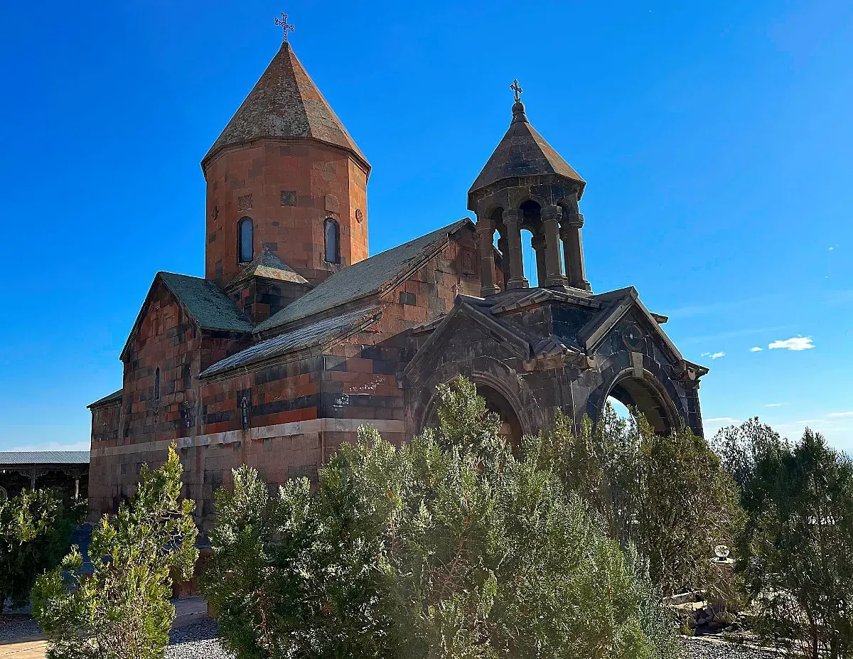 Red-tinted stone monastery against an almost cloud-less sky