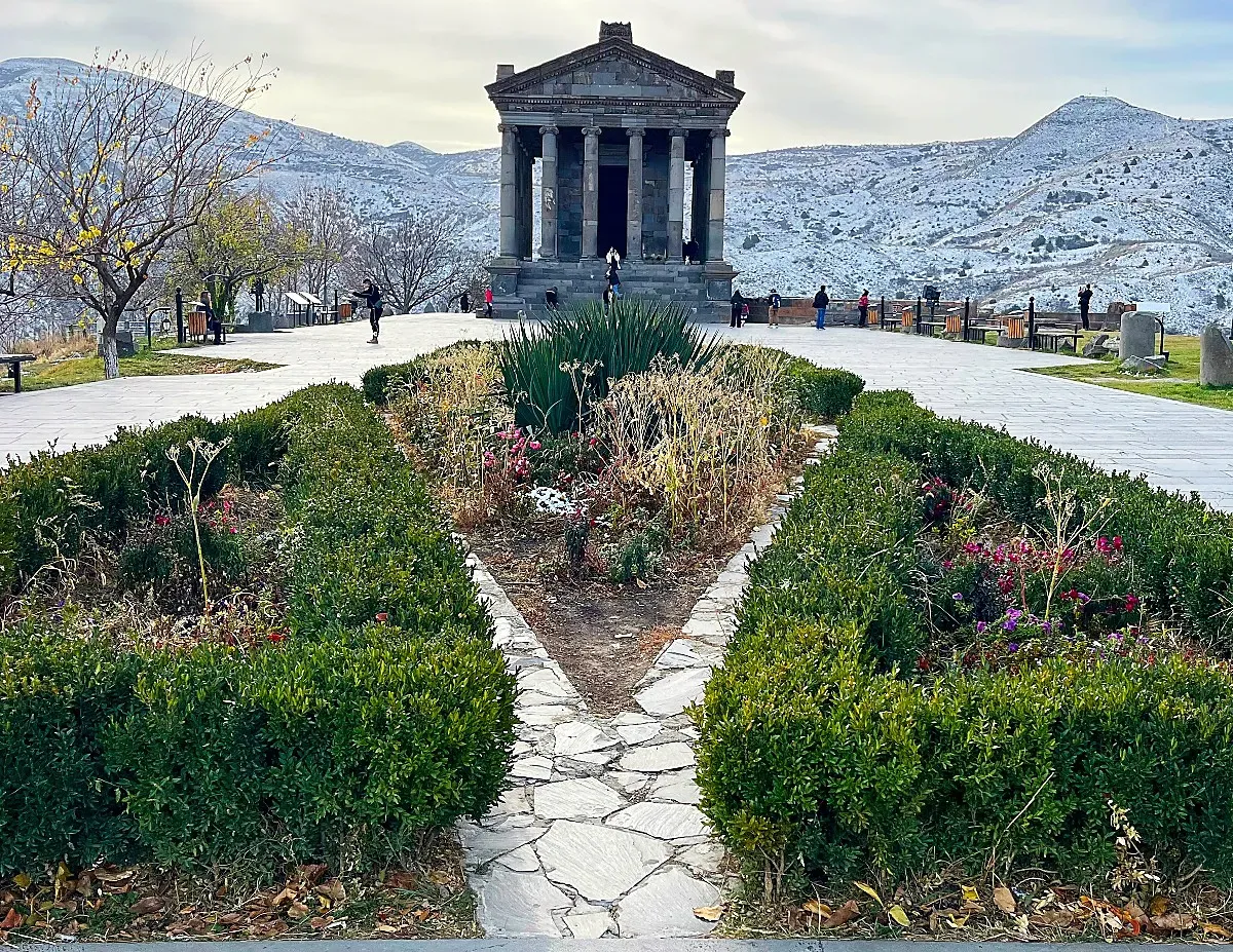 Shrubs in the foreground with a temple six-columns wide at the center with snowy mountains in the background