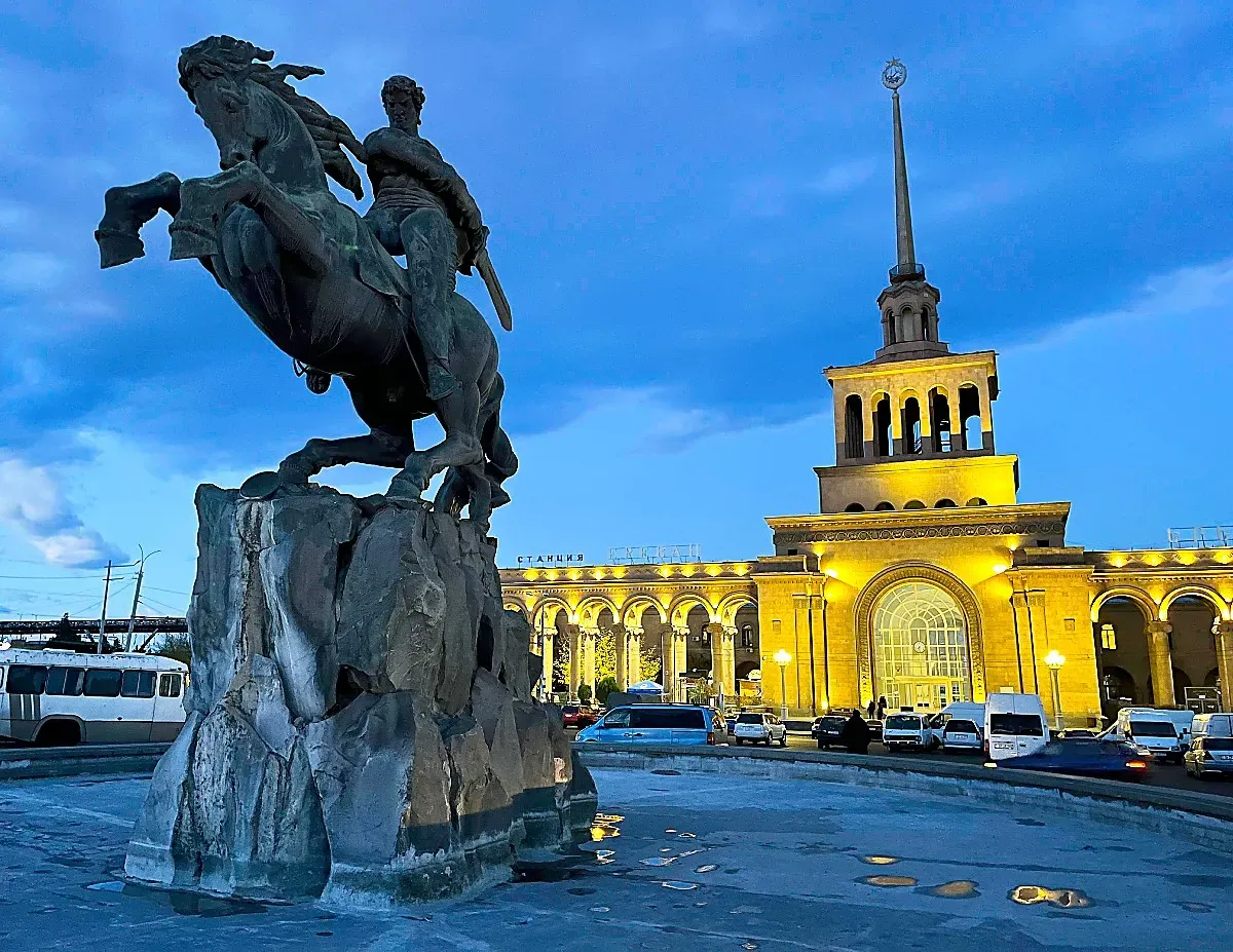 Statue of mounted man in front of a lit-up railway station