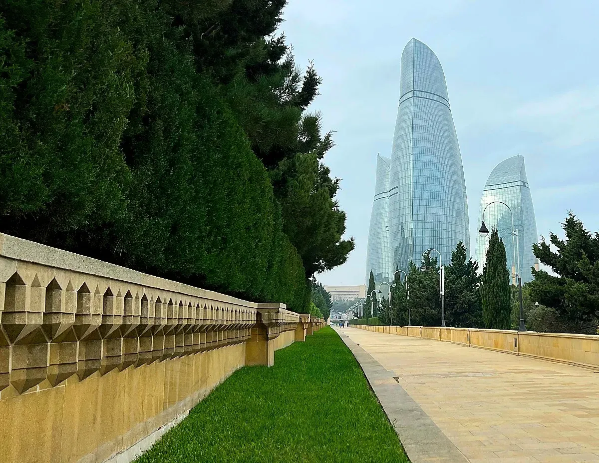 Stone walkway lined with trees pointed at three glass skyscrapers
