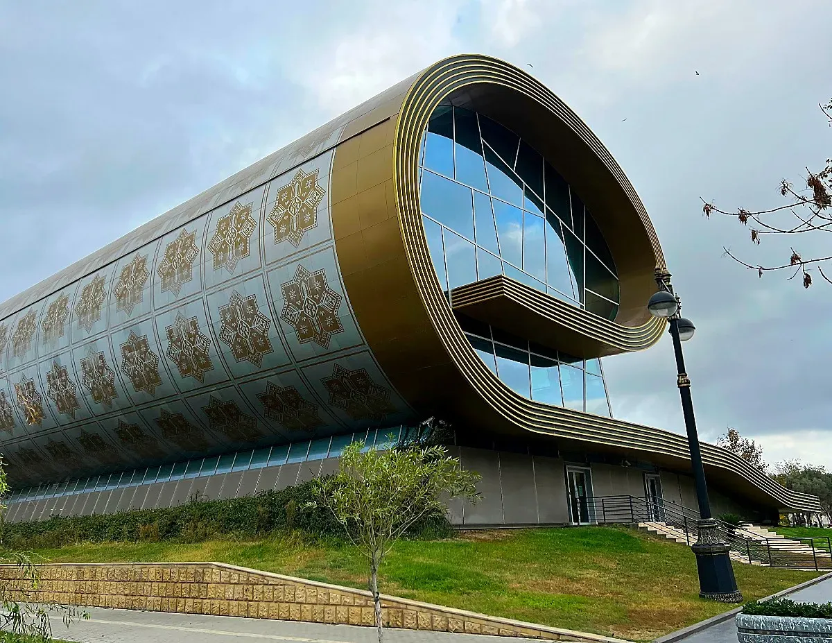 Glass building in the shape of a partially rolled carpet