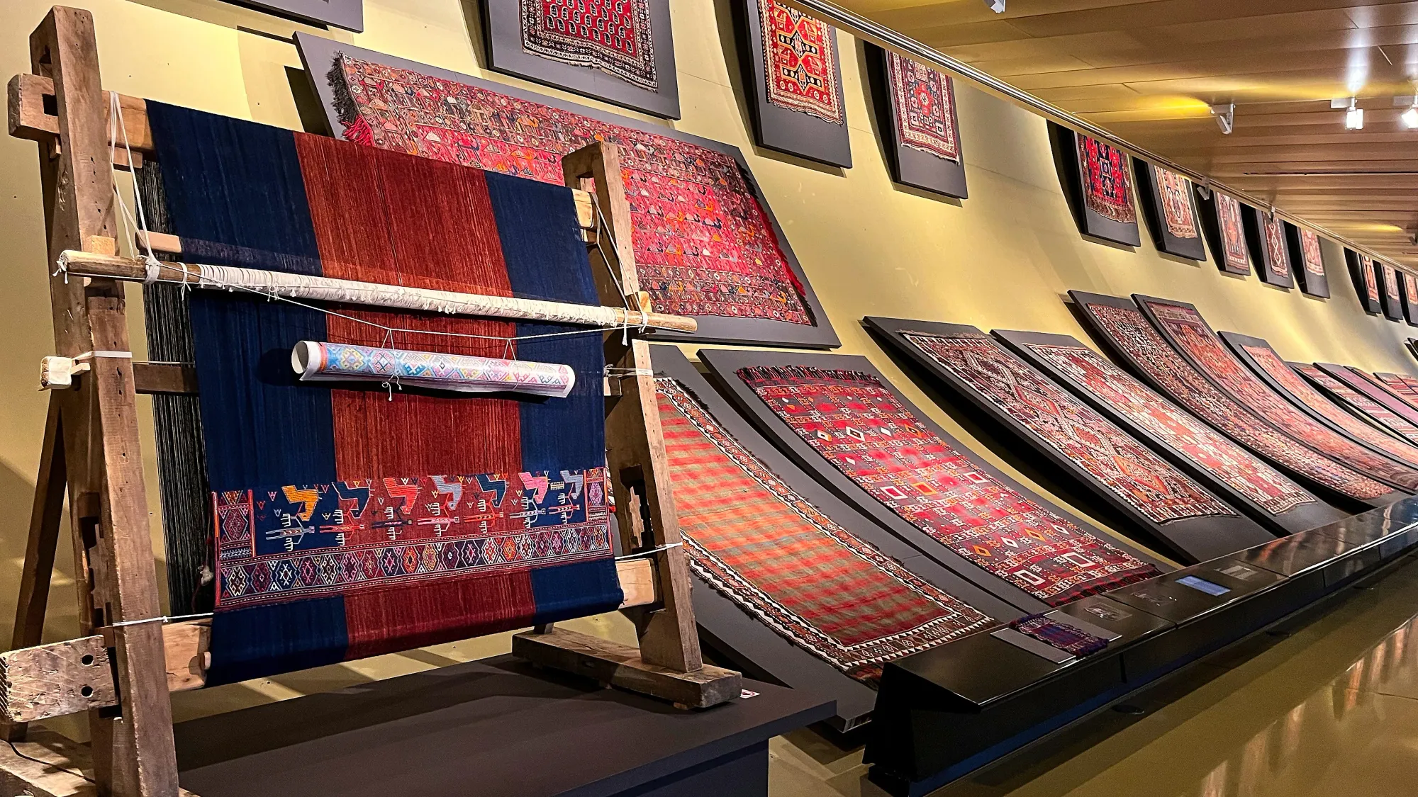 A loom in progress alongside a wall full of mounted woven carpets
