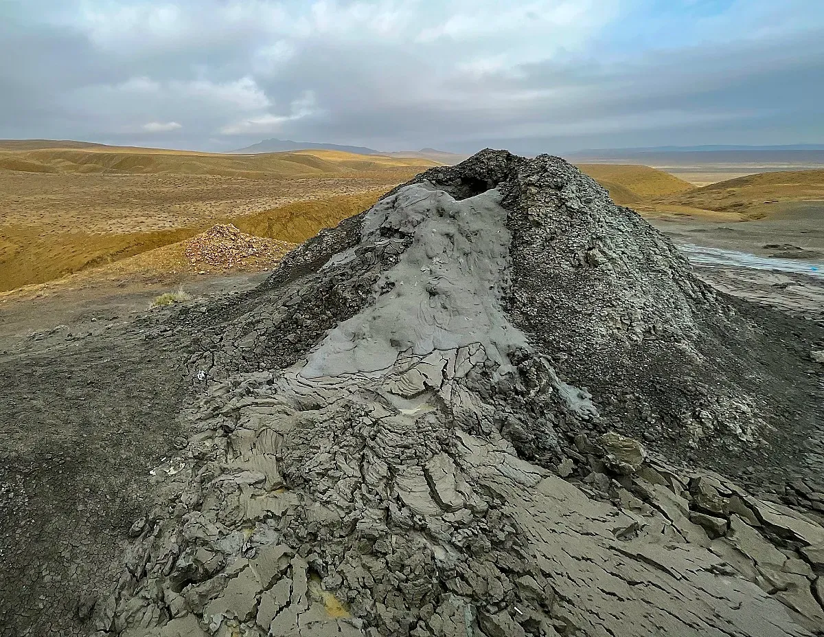 Grey mound of coagulated grey mud billowing out of the top of the volcano