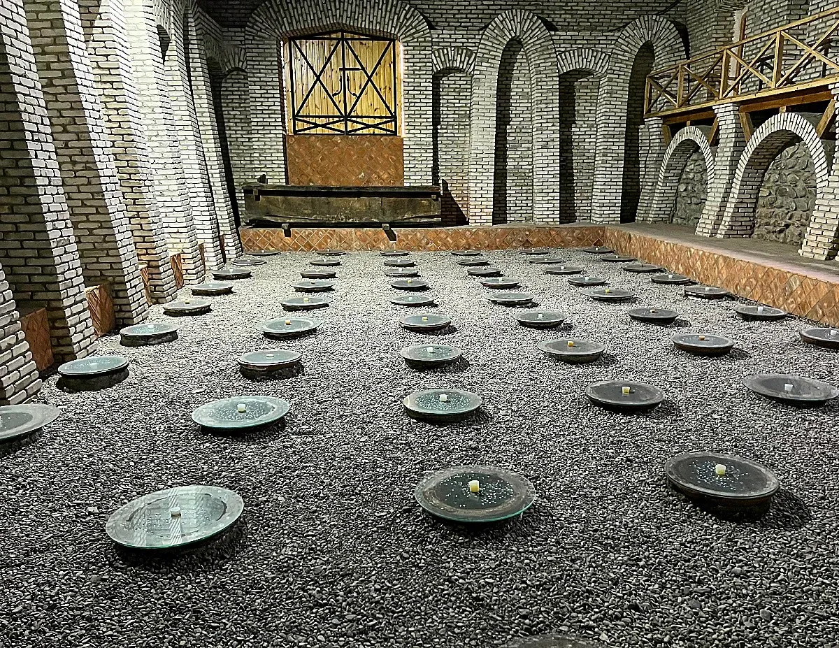 Dozens of round lids sitting on clay wine jugs burried under a gravel floor in a white brick rooom