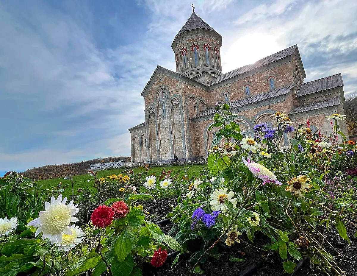 Flowers obscure the foreground and a stone monastery rests in the background