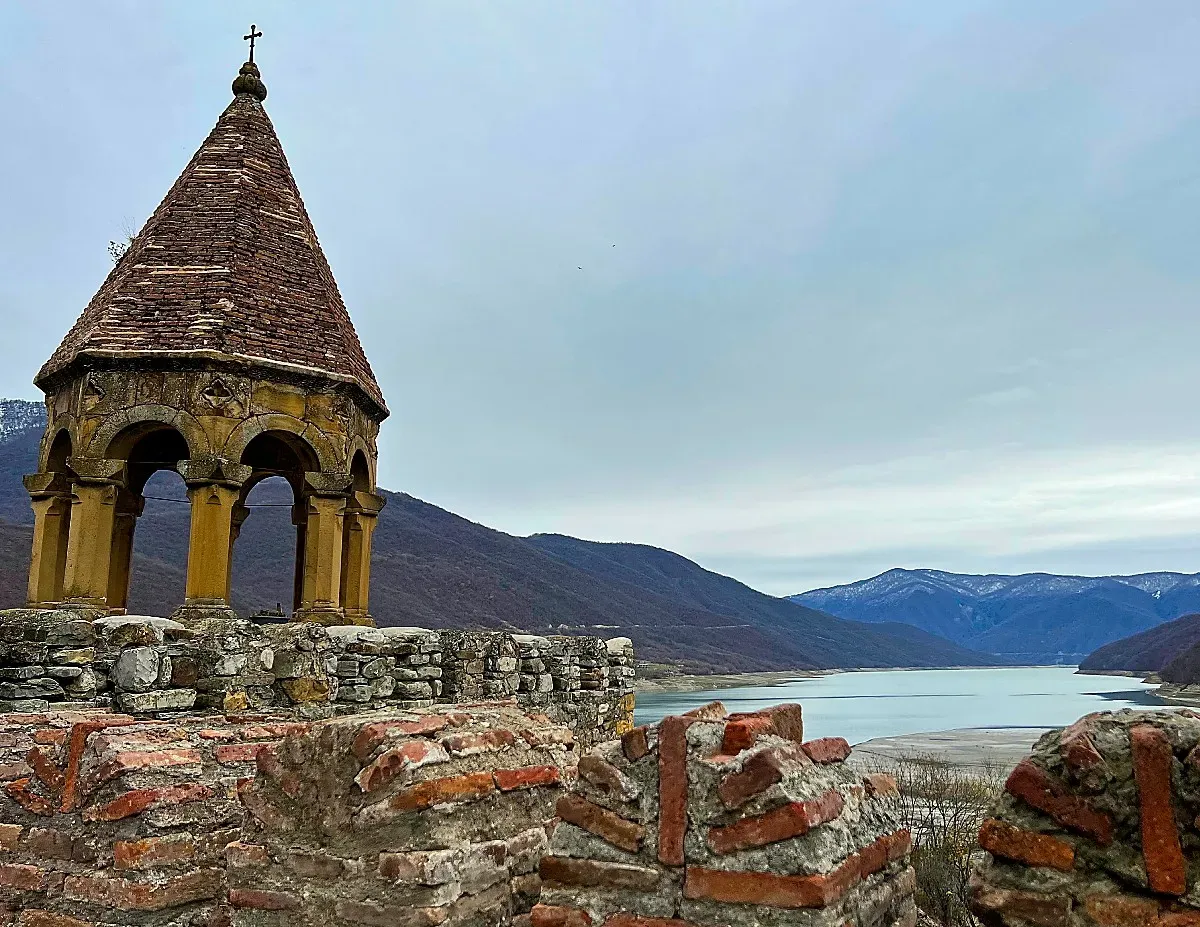 Arched gazebo atop a stone wall overlooking a lake