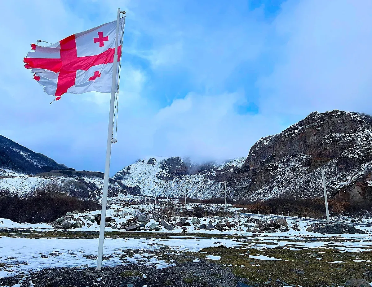 Tattered Georgian flag blowing before snowy mountains