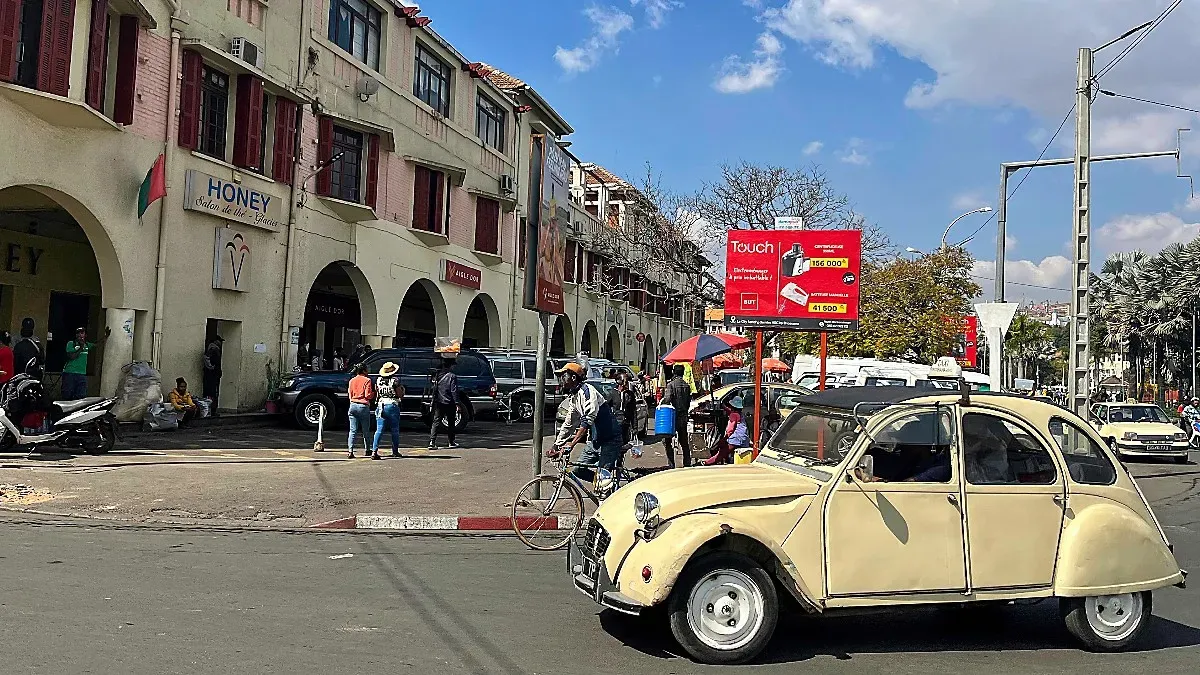 Old yellow car driving next to an arched shopping center