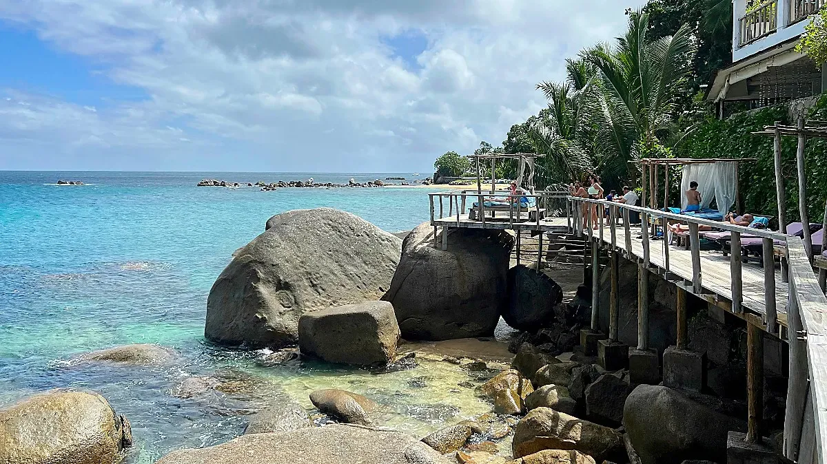 Large boulders bolster a wooden deck with sun beds overlooking the ocean