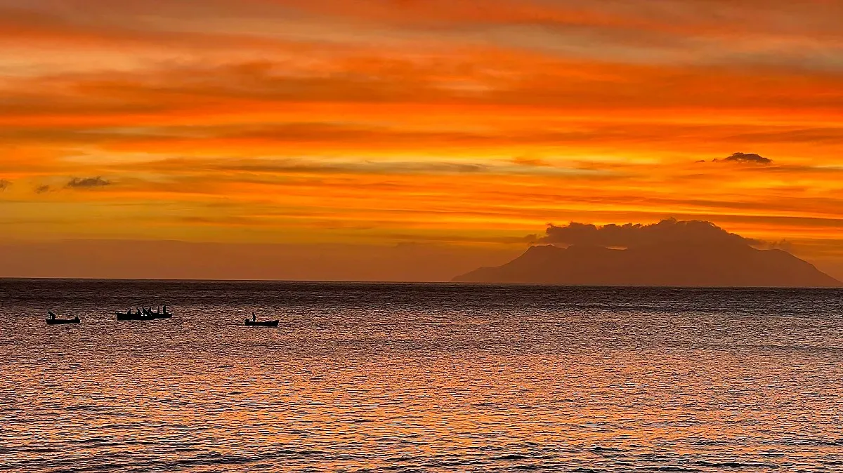 Very orange sky with silhouettes of boys on row boats in the water