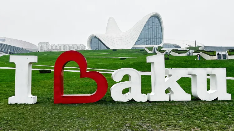 A three dimensional "I Heart Baku" sign in white located on a grassy lawn in front of a curved white building