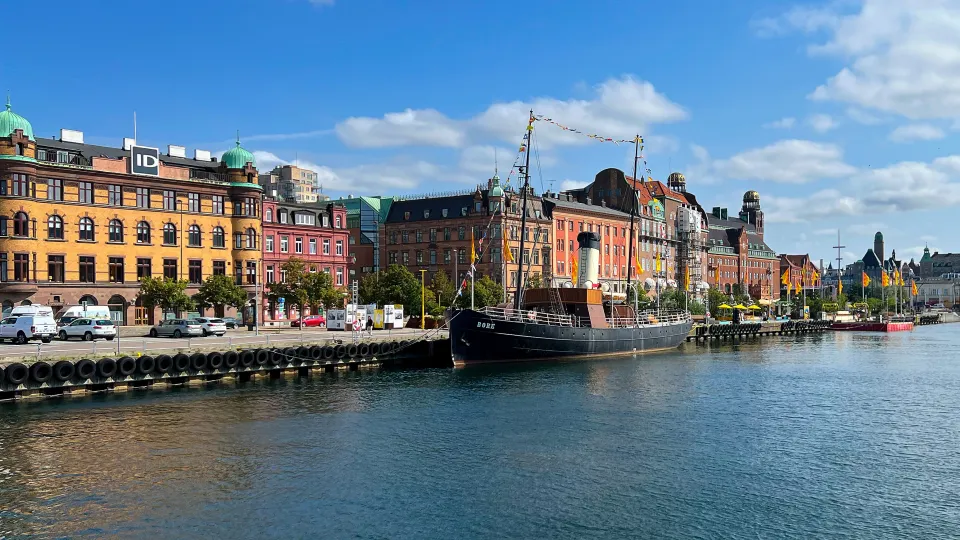 Waterfront with a black ship, yellow/pink/orange buildings, and lots of flags